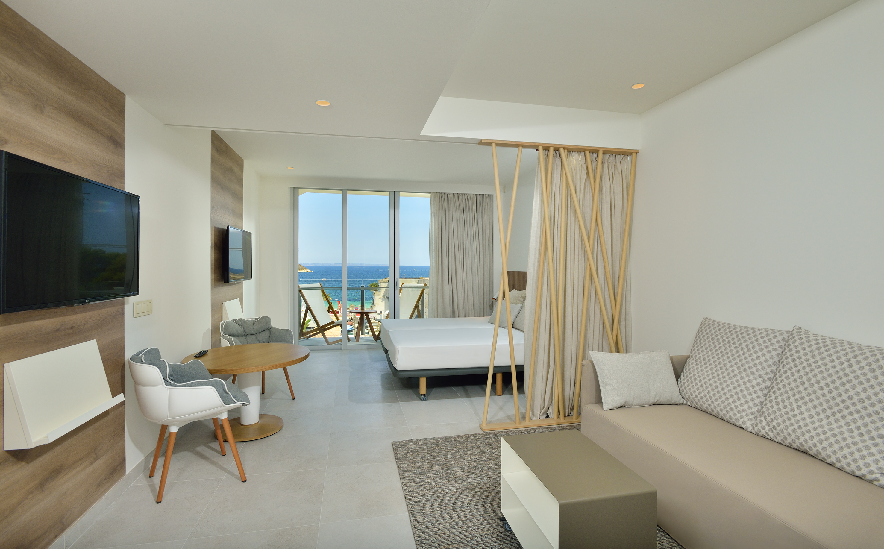 Modern hotel room with sea view balcony, bed, sofa, and dining area.