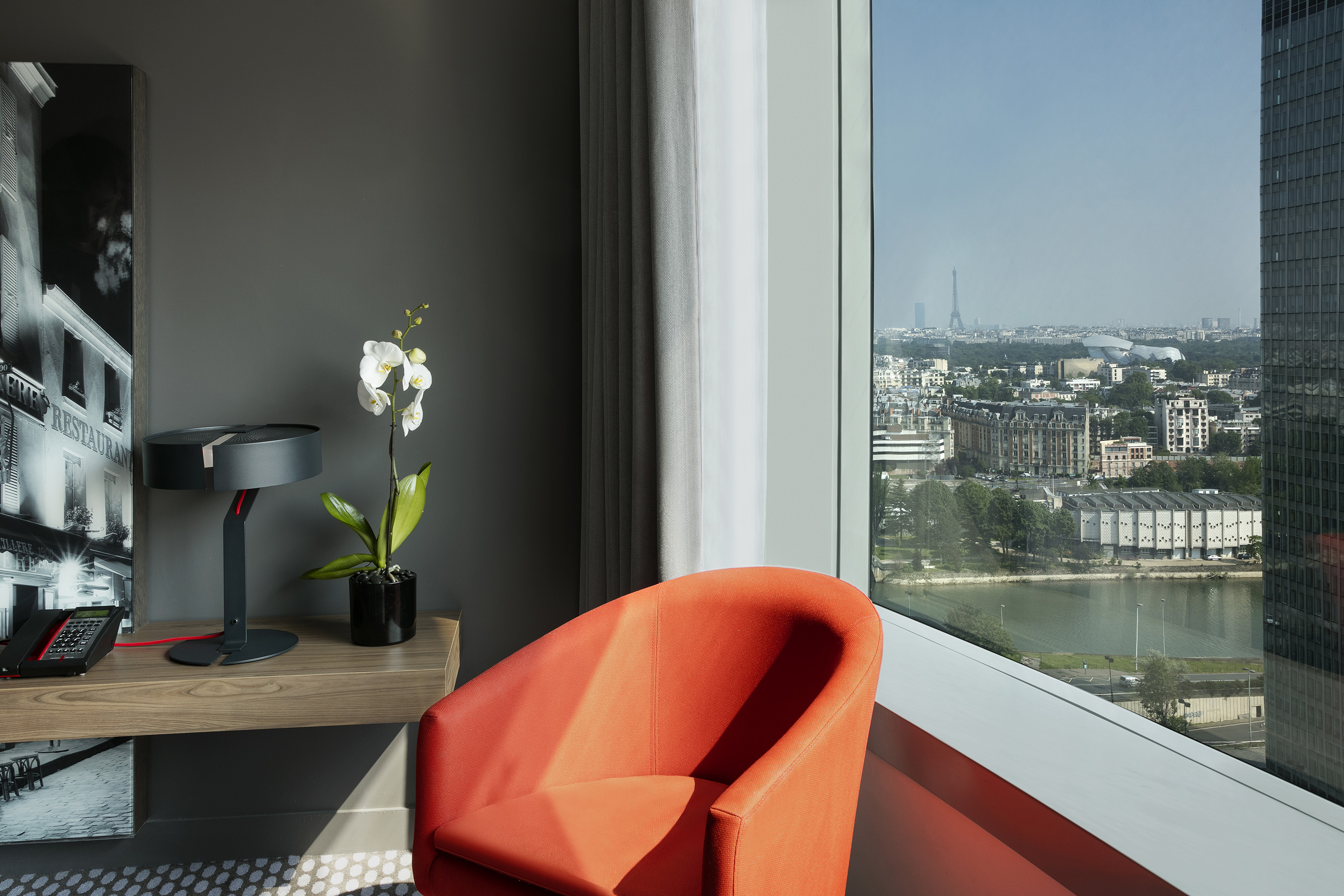 Orange armchair in modern room with Paris city view, Eiffel Tower in distance.