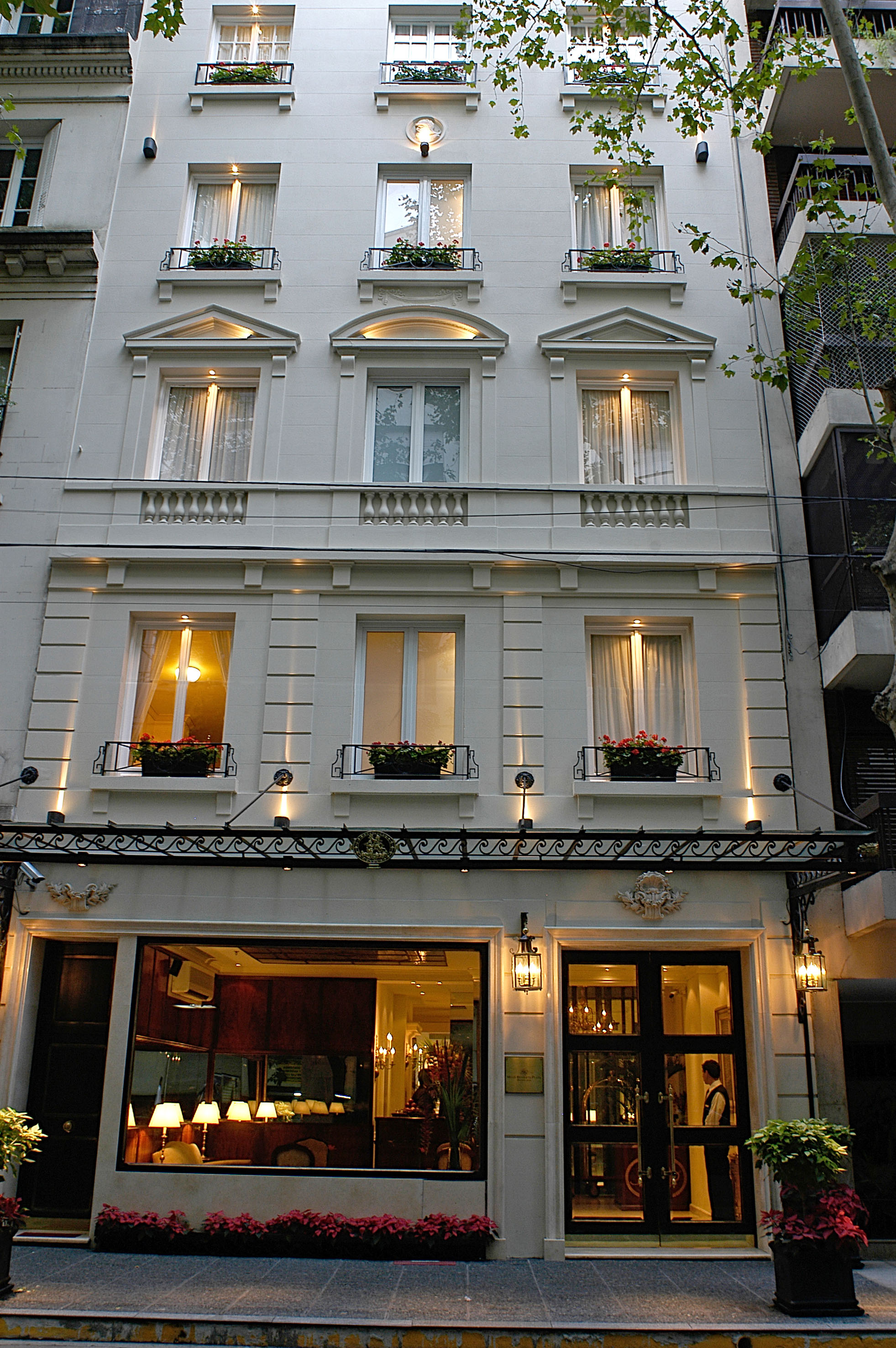 Classical hotel building facade with illuminated windows, flower boxes, and entrance.