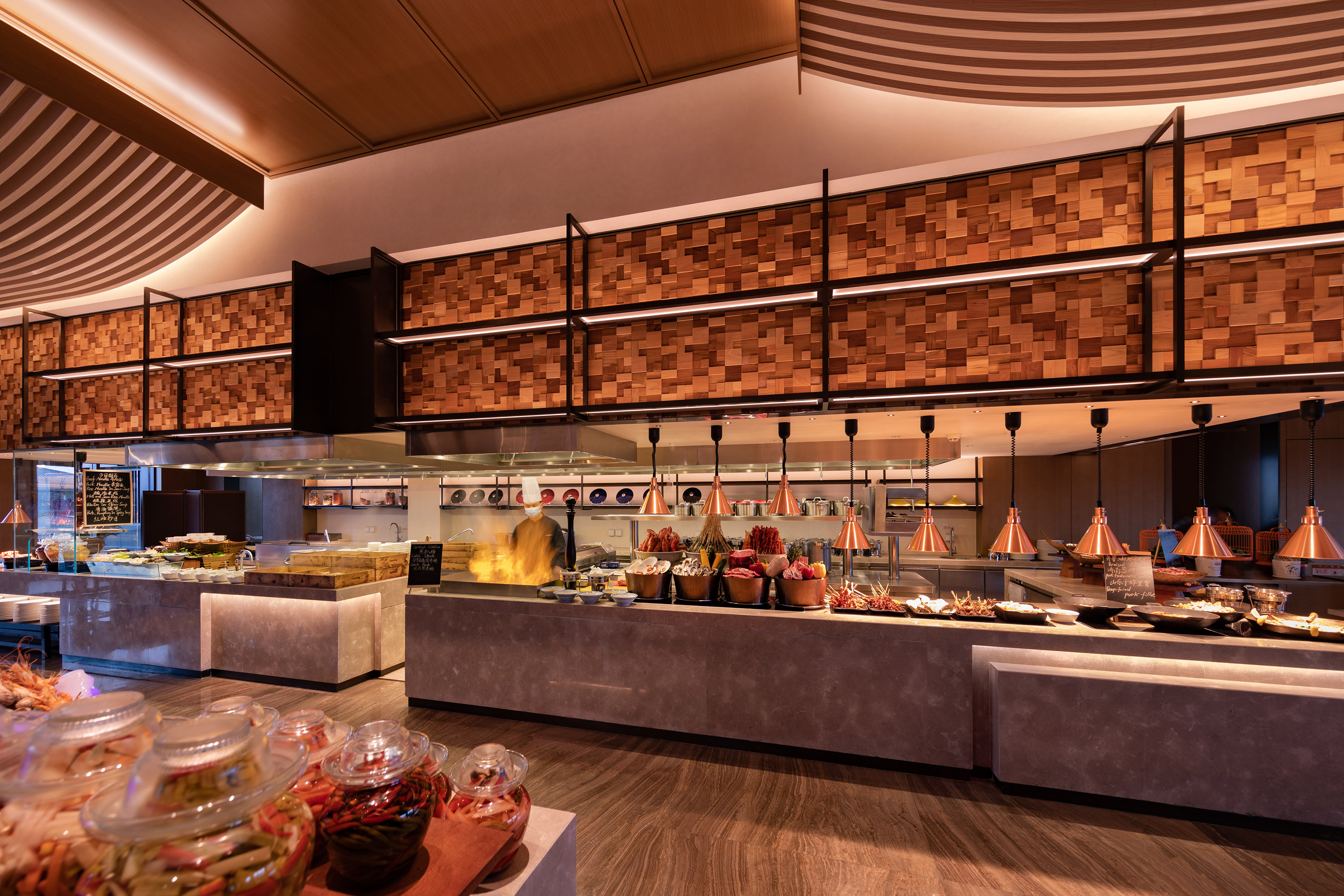 Modern buffet restaurant with open kitchen, chef cooking, and diverse food displays.
