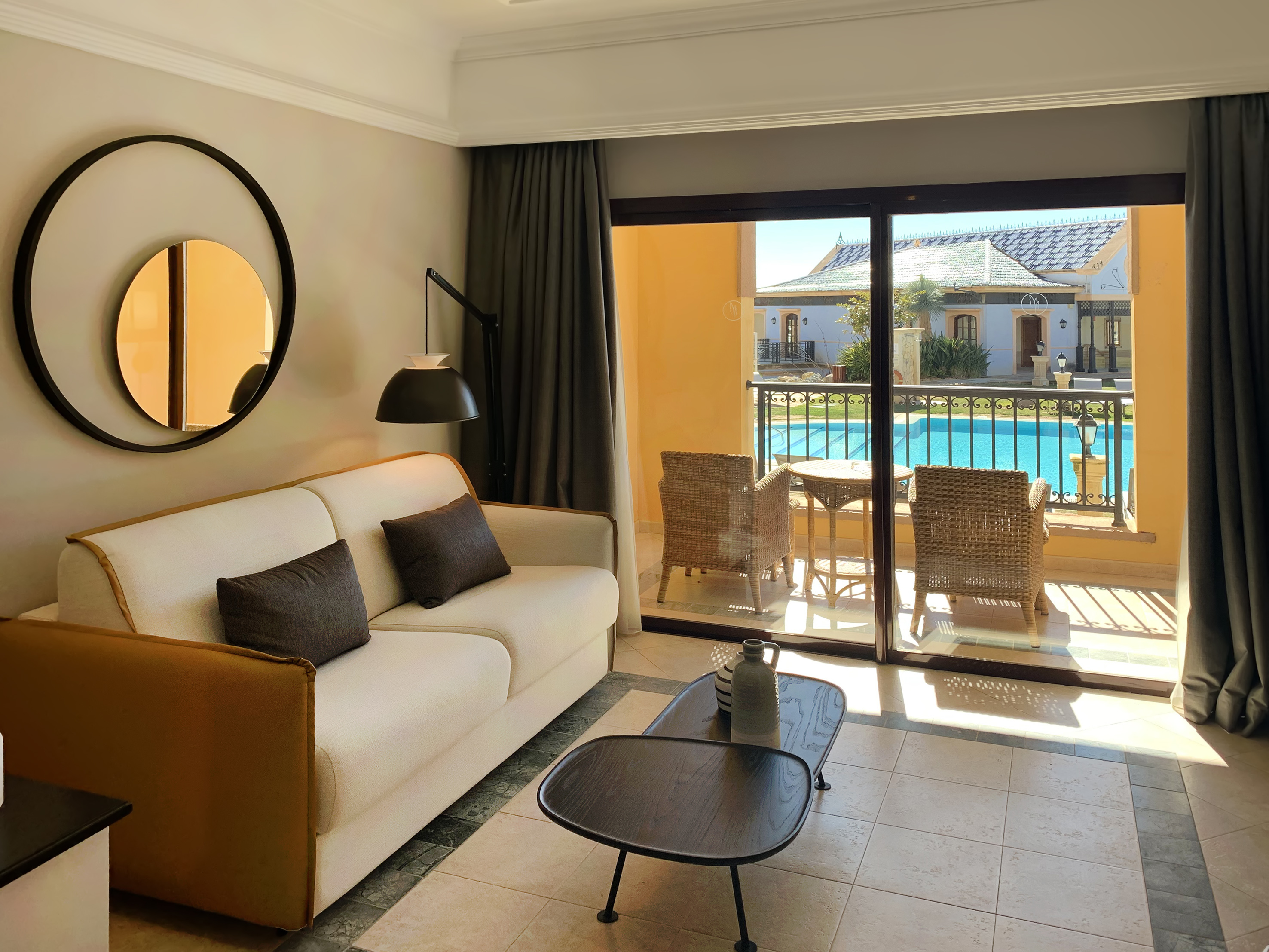 Modern living room with sofa, balcony, and pool view in a resort suite.