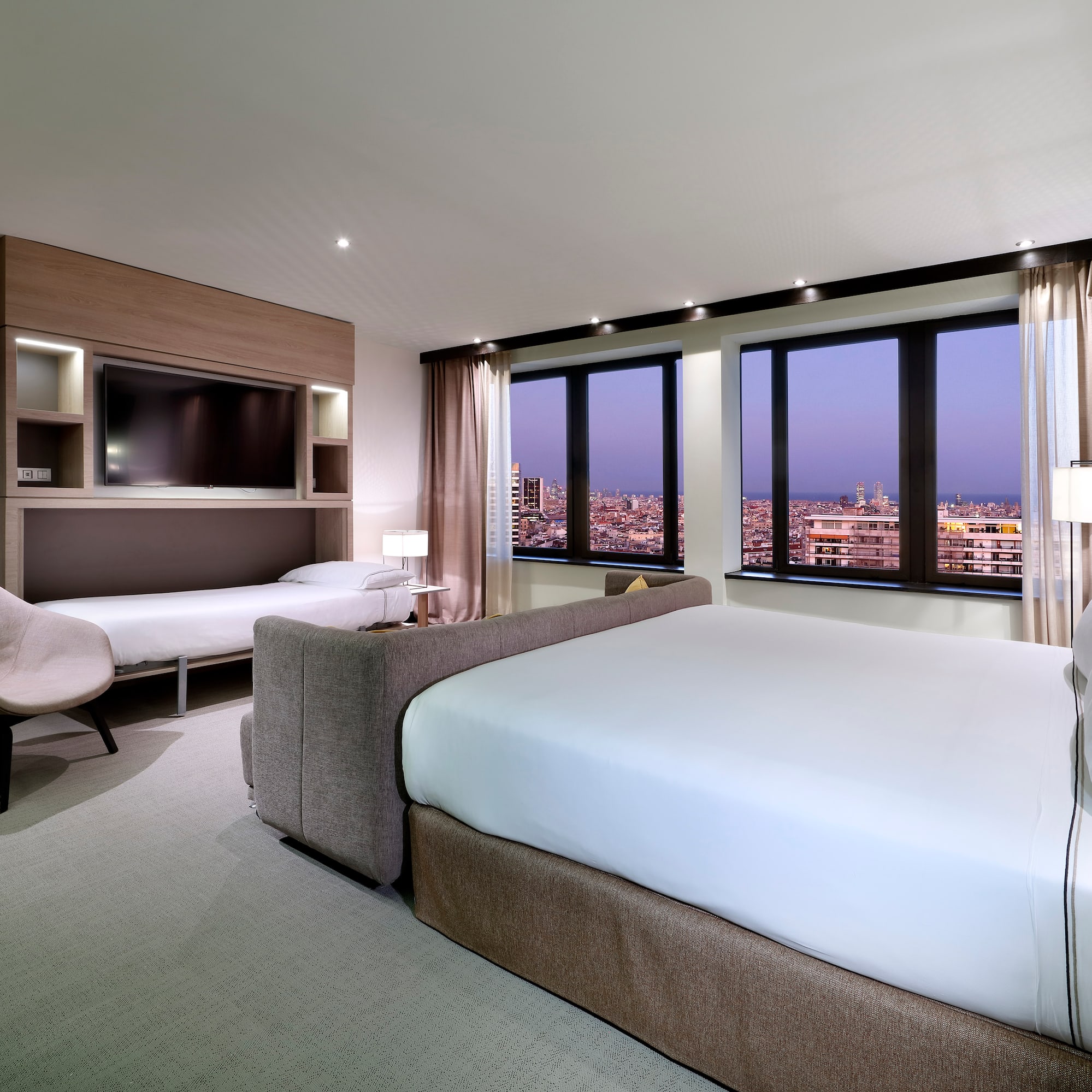 Modern hotel room with city night view, large bed, and integrated fold-down bed.