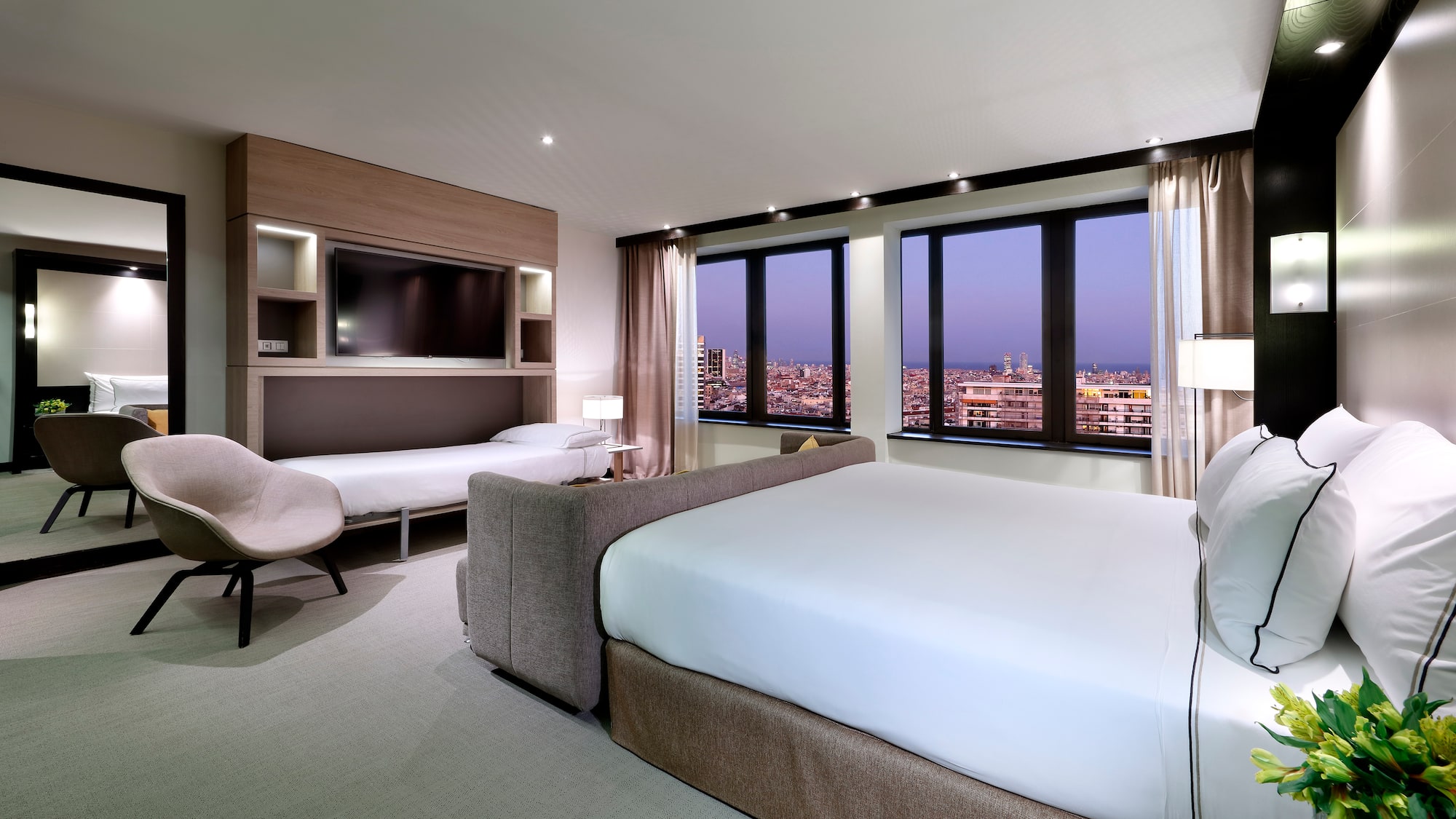 Modern hotel room with city night view, large bed, and integrated fold-down bed.
