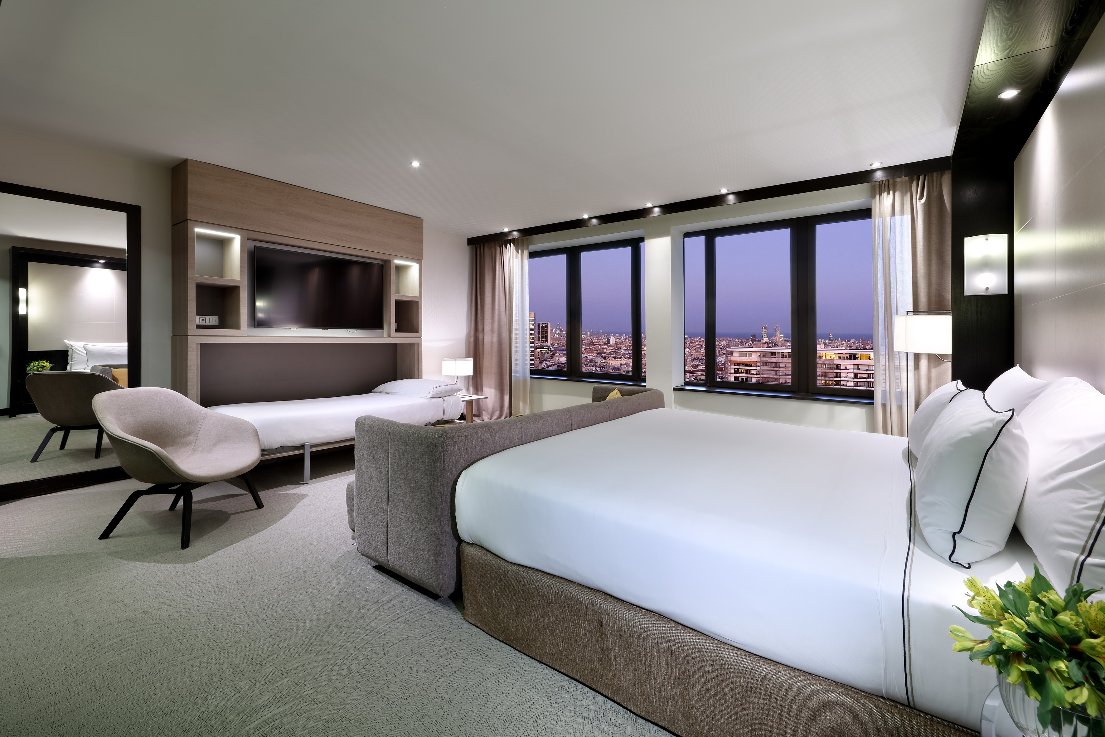 Modern hotel room with city night view, large bed, and integrated fold-down bed.