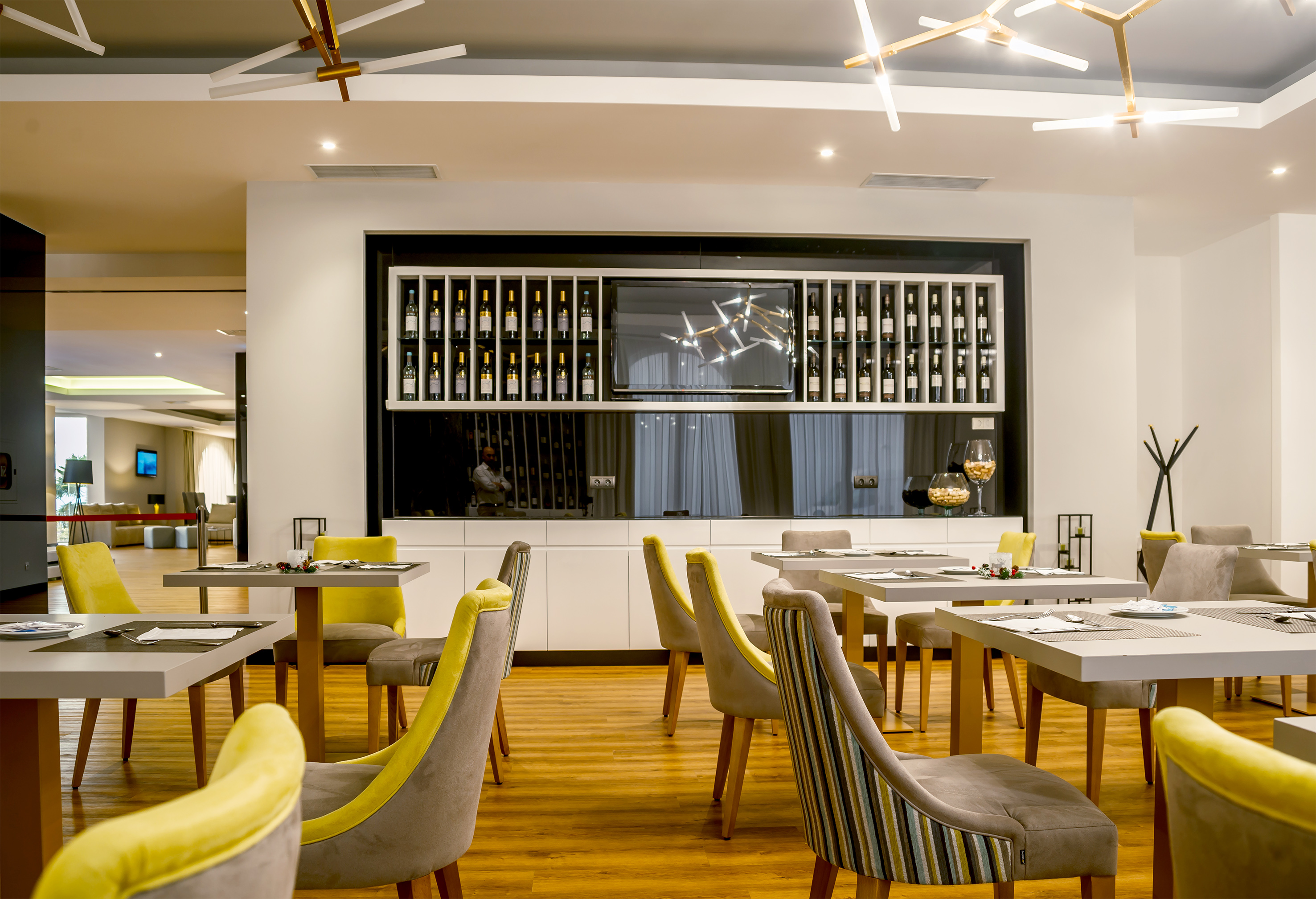Modern restaurant dining room with wine display wall, yellow chairs, and tables.