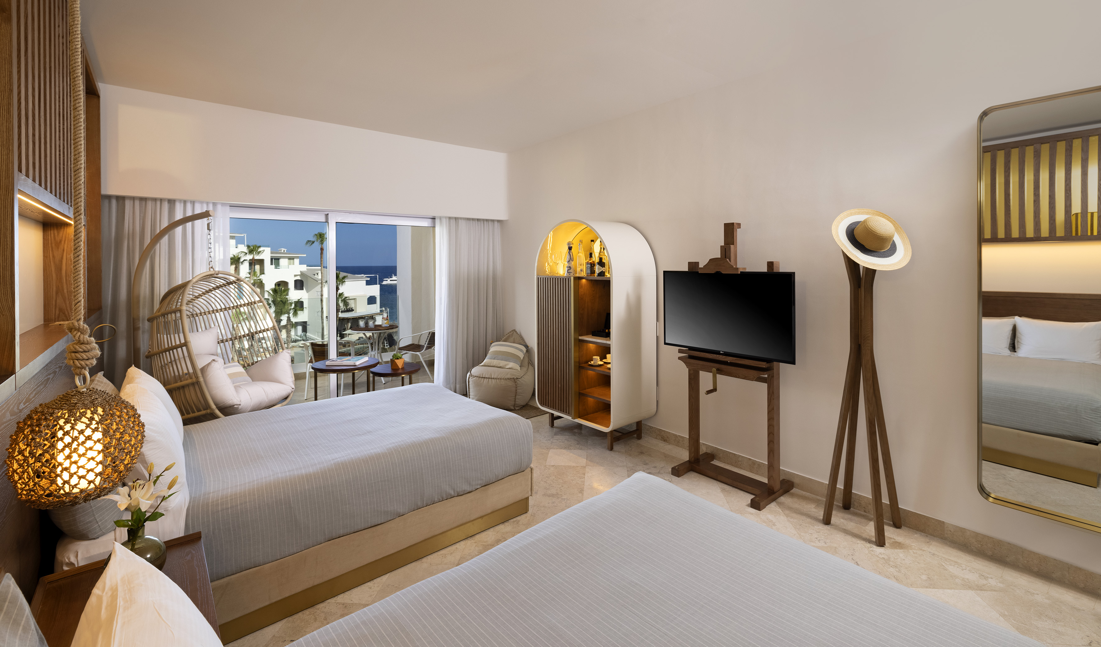 Coastal hotel room, ocean view balcony, two beds, wicker hanging chair.