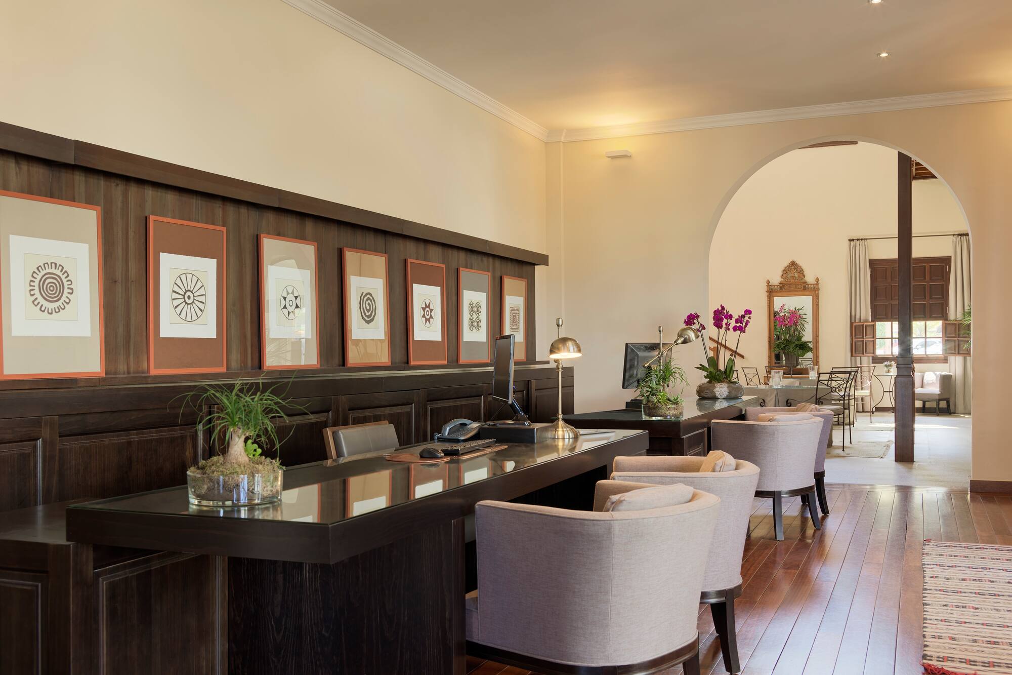 Modern hotel reception area with dark wood desk, framed art, and seating.
