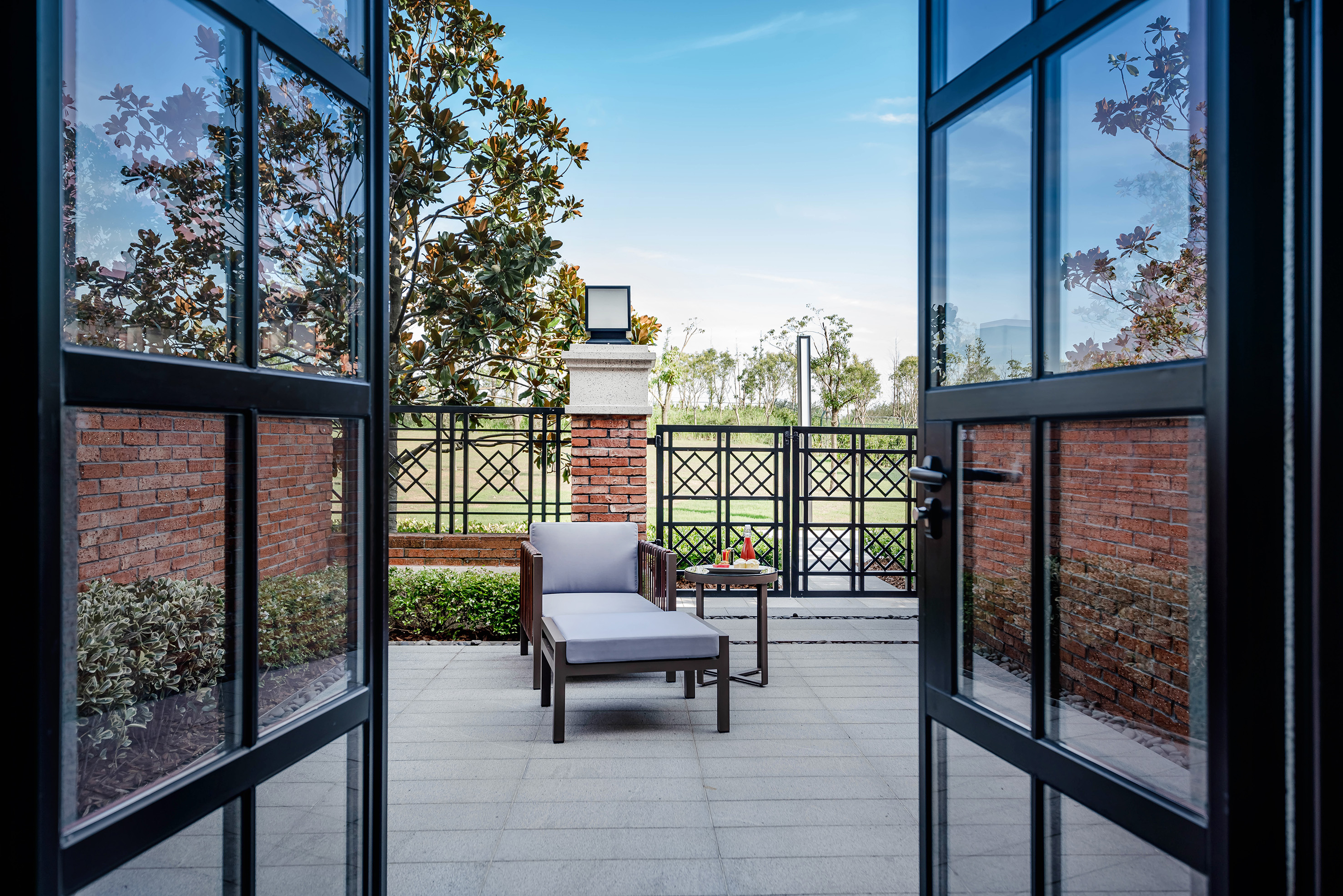 Open French doors to modern patio with chaise lounge, side table, and garden view.