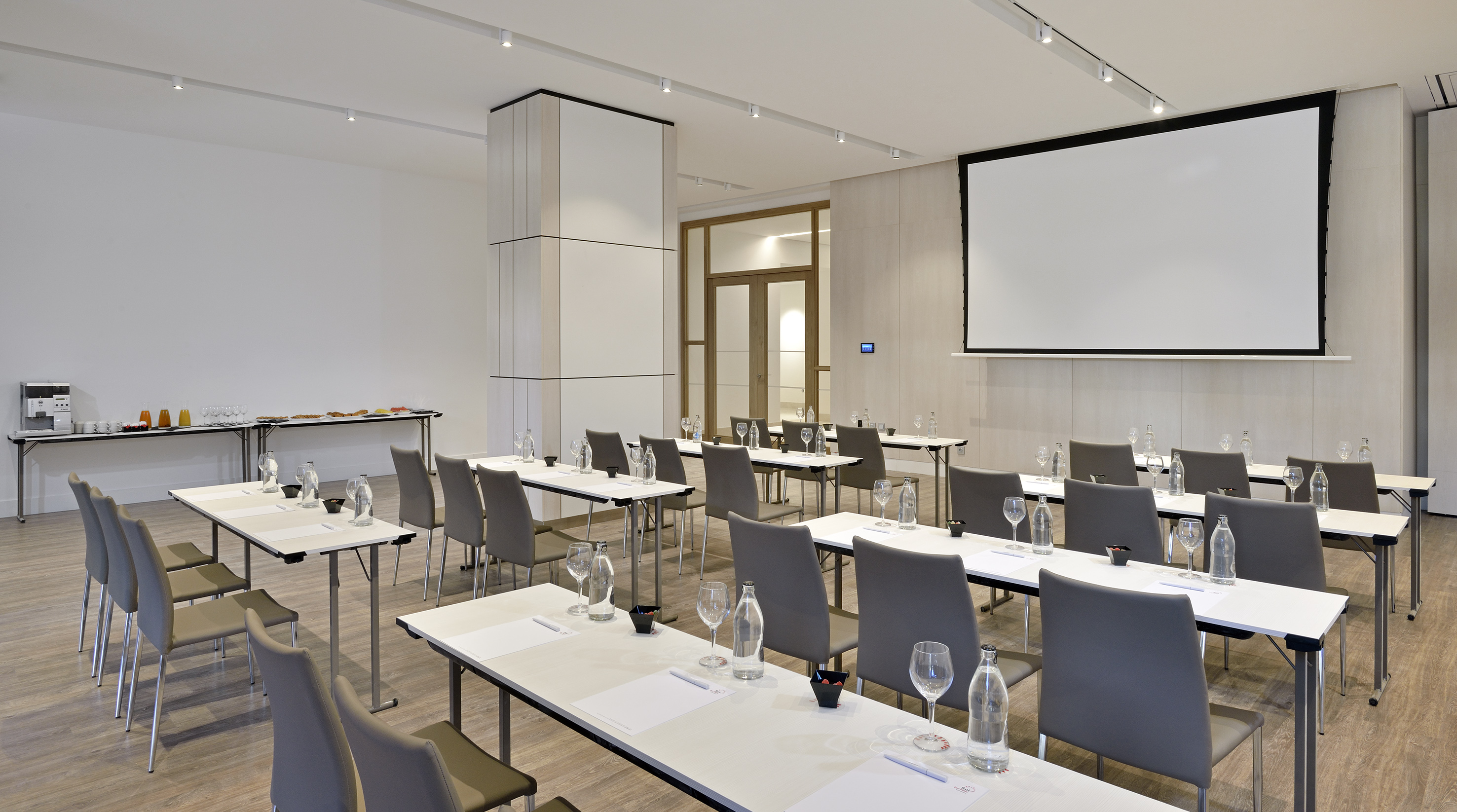 Modern classroom-style meeting room with screen and beverage service.