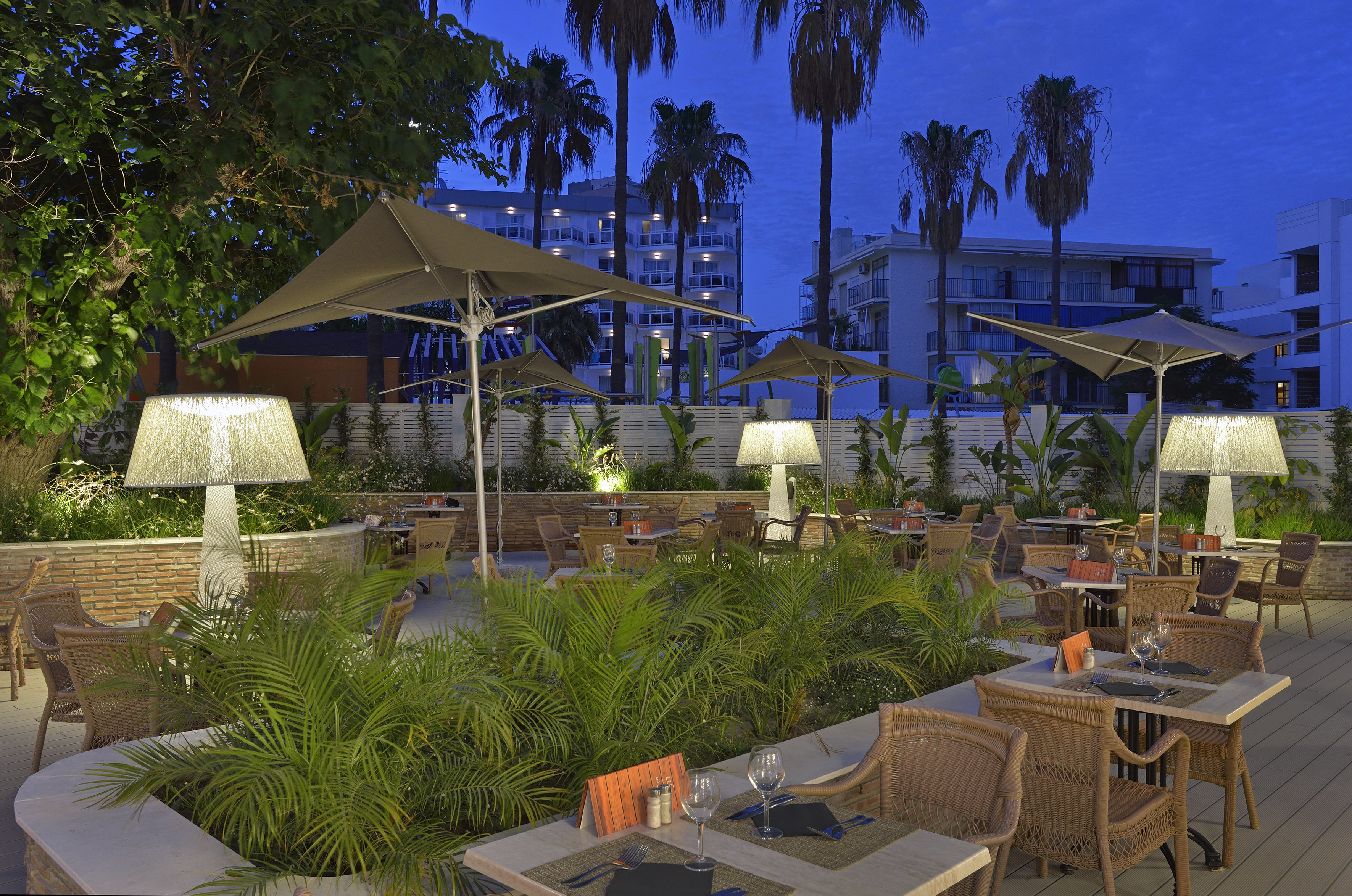 Illuminated outdoor restaurant patio with palm trees and set dining tables.