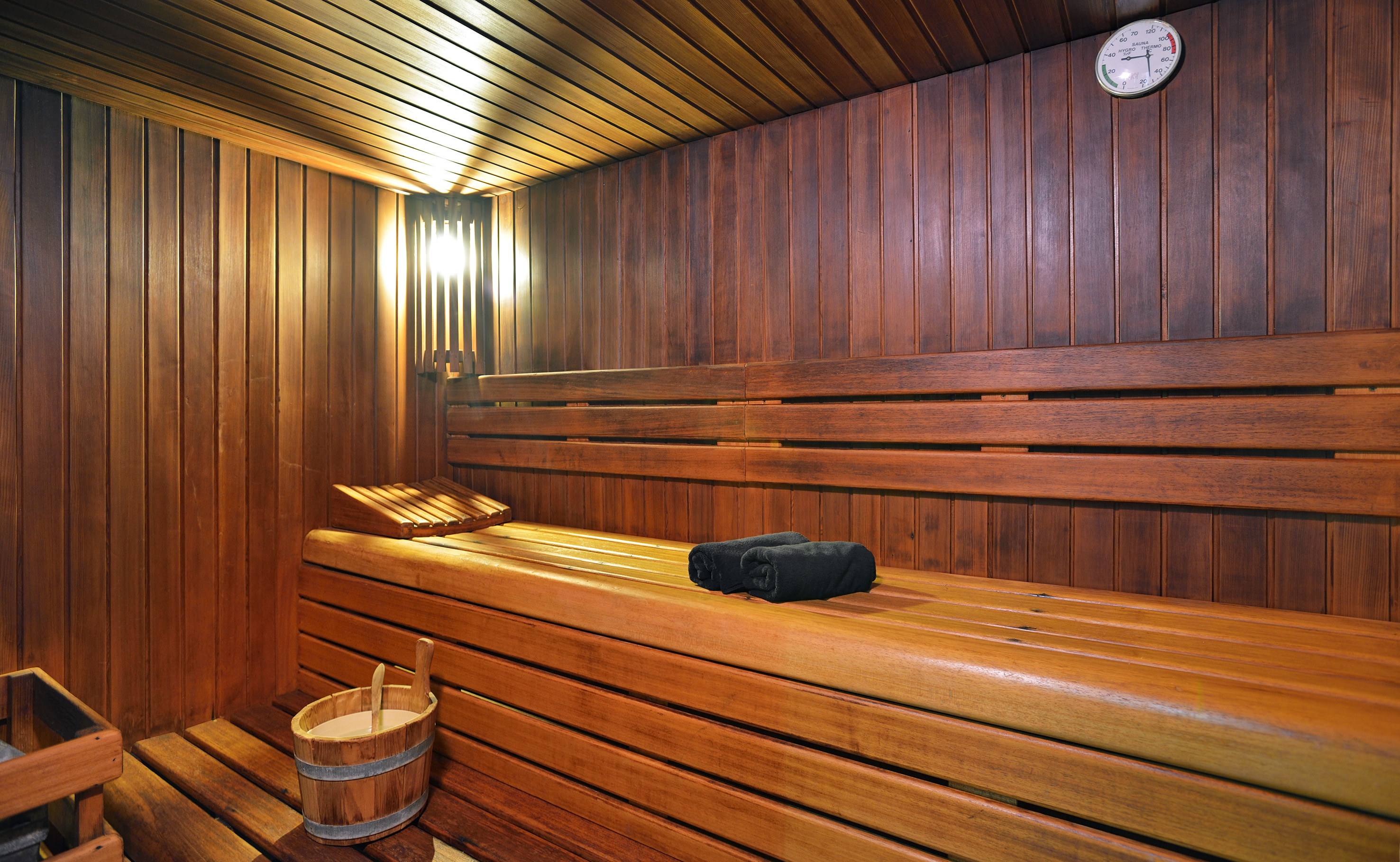 Empty wooden sauna with warm lighting, benches, bucket, and towels. - Area benessere - Meliá Cala d'Or Boutique Hotel, Maiorca
