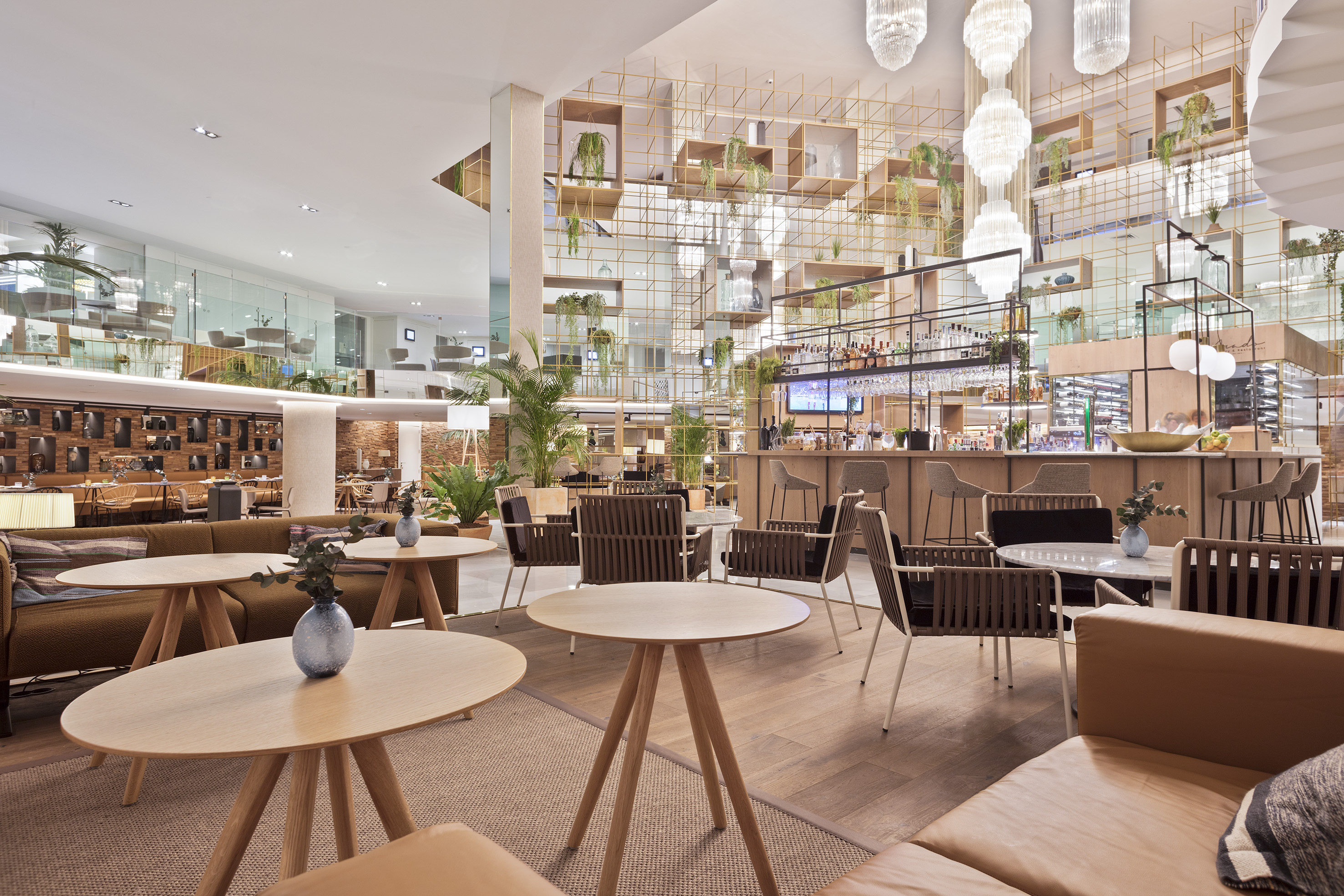 Modern hotel lounge bar with various seating, green plants, and chandeliers.