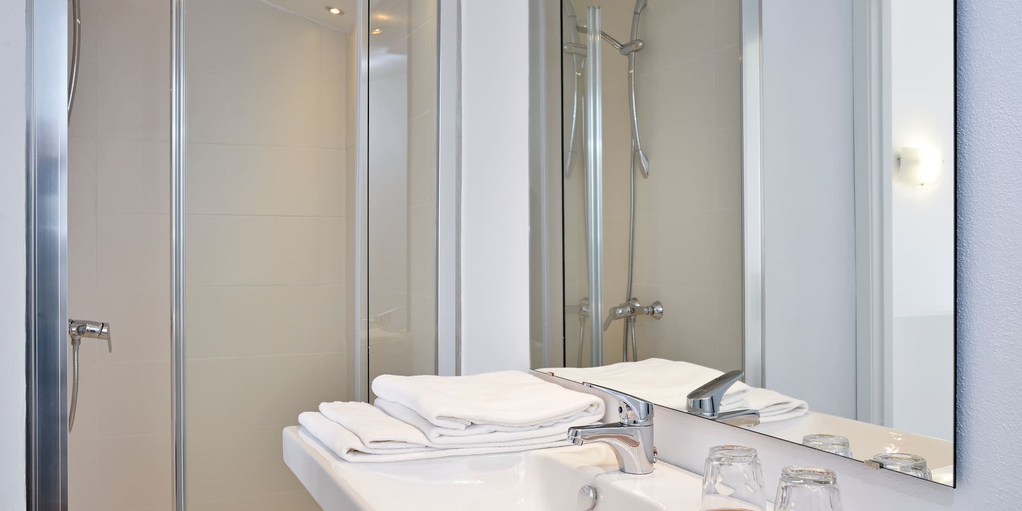 Modern bathroom with walk-in glass shower, white sink, and folded towels.