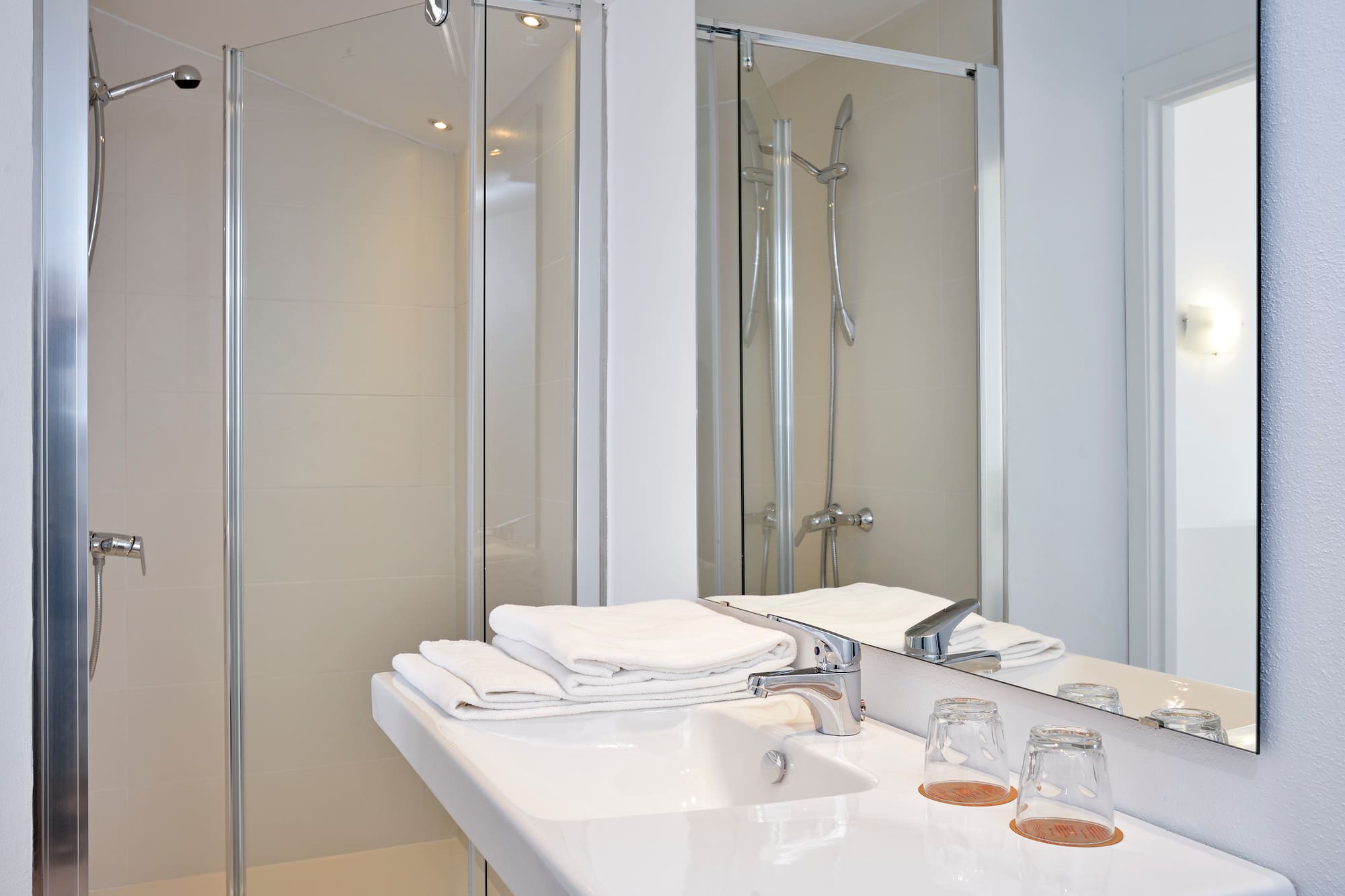 Modern bathroom with glass shower, white sink, chrome faucet, and clean towels.
