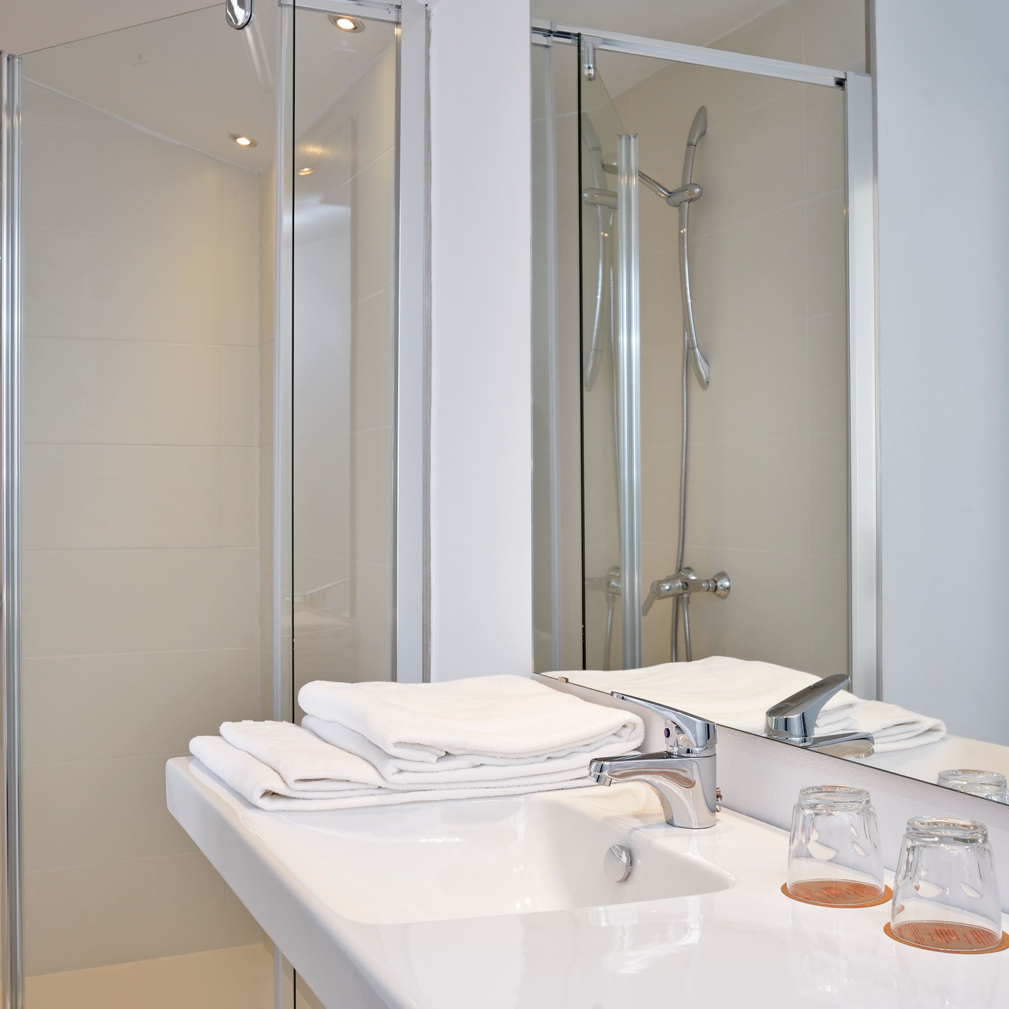 Clean modern bathroom with white sink, faucet, towels, and glass shower.