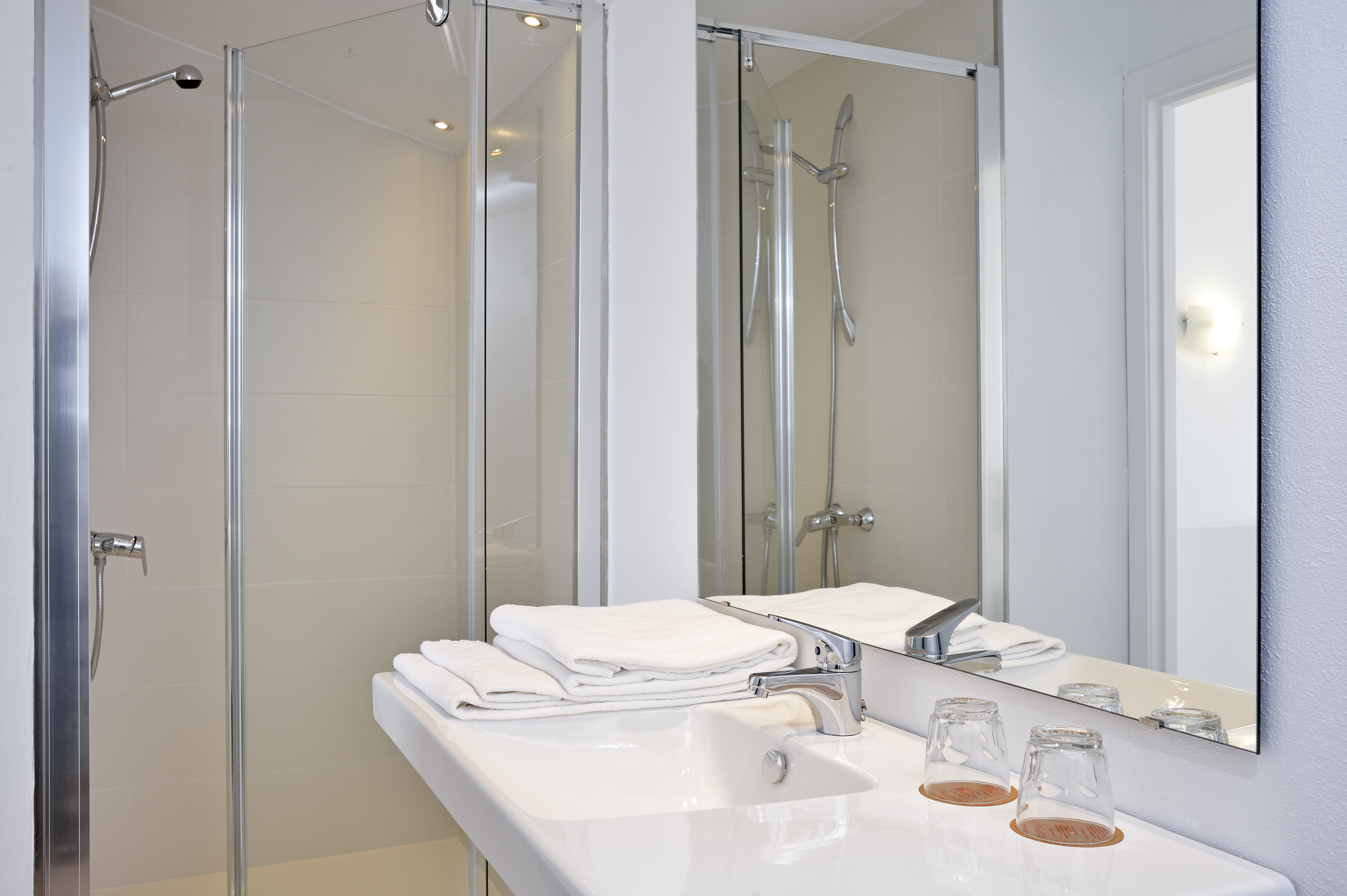 Modern bathroom with glass shower, white sink, chrome faucet, and clean towels.