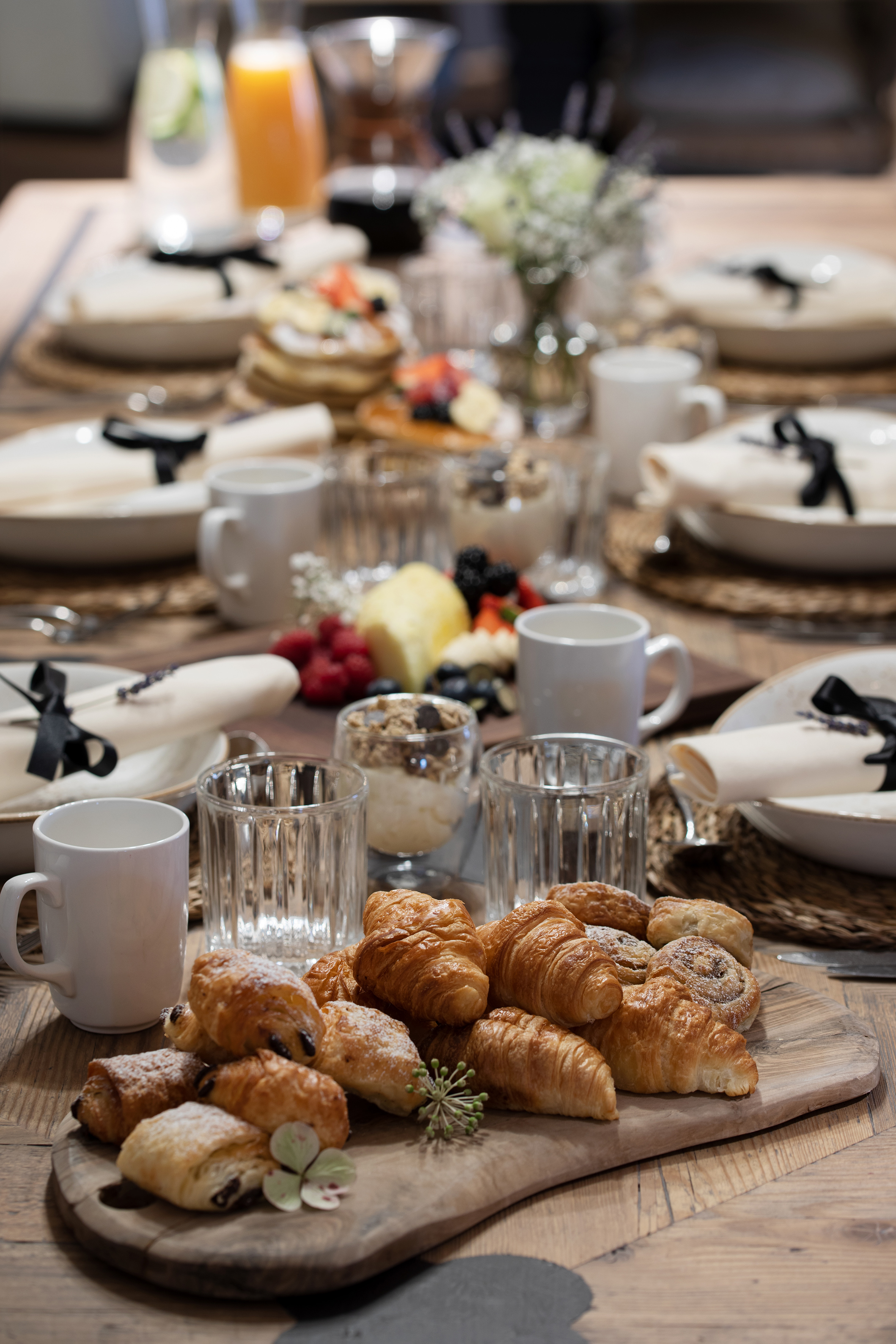 Gourmet brunch table filled with croissants, fresh fruit, pancakes, and drinks.