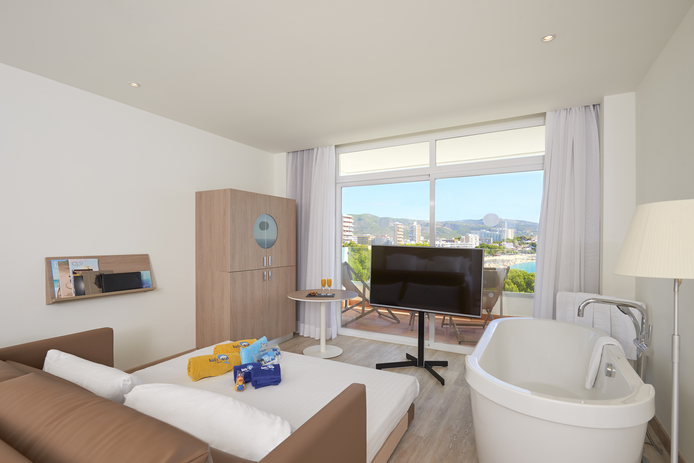 Family hotel room with sofa bed, tub, TV, and beach view balcony.