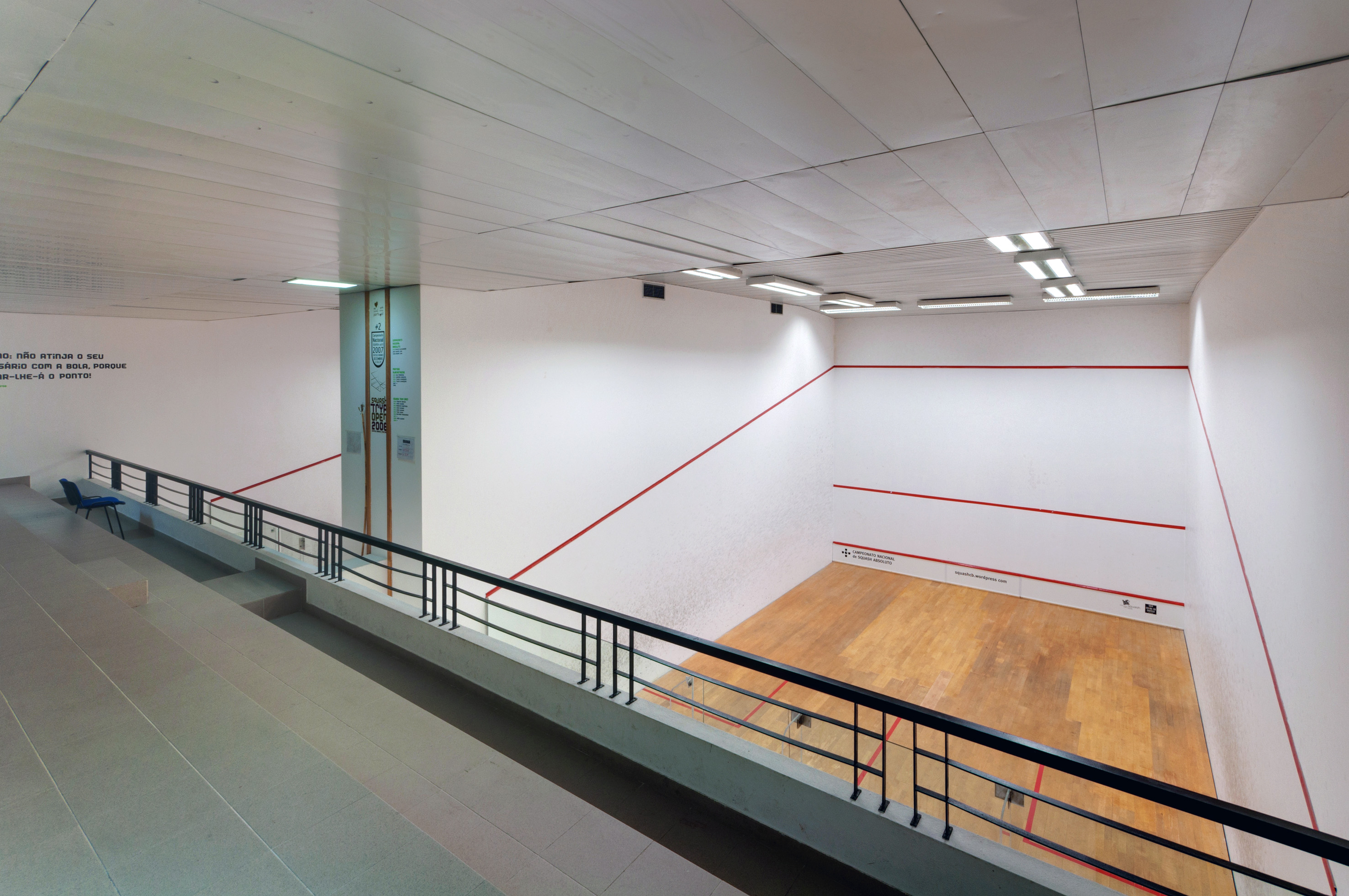 Elevated view of an empty indoor squash court with white walls, red lines, and wooden floor.