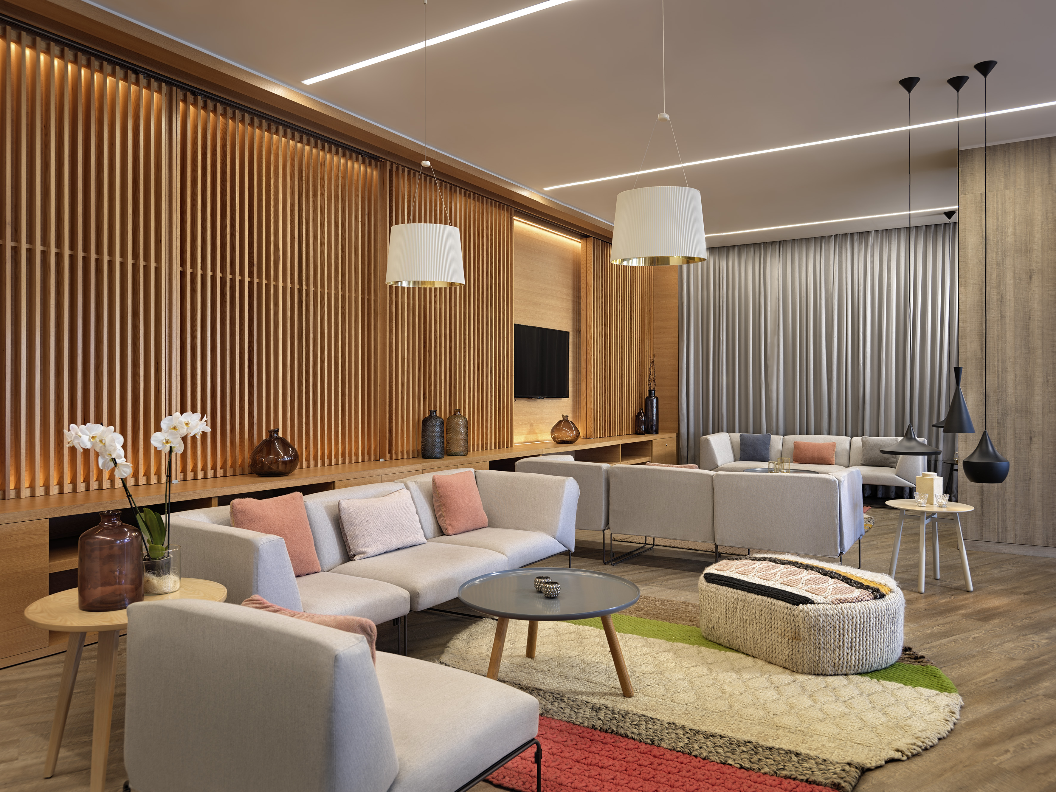 Modern lounge with modular sofas, wooden slat wall, colorful rug, pendant lighting.