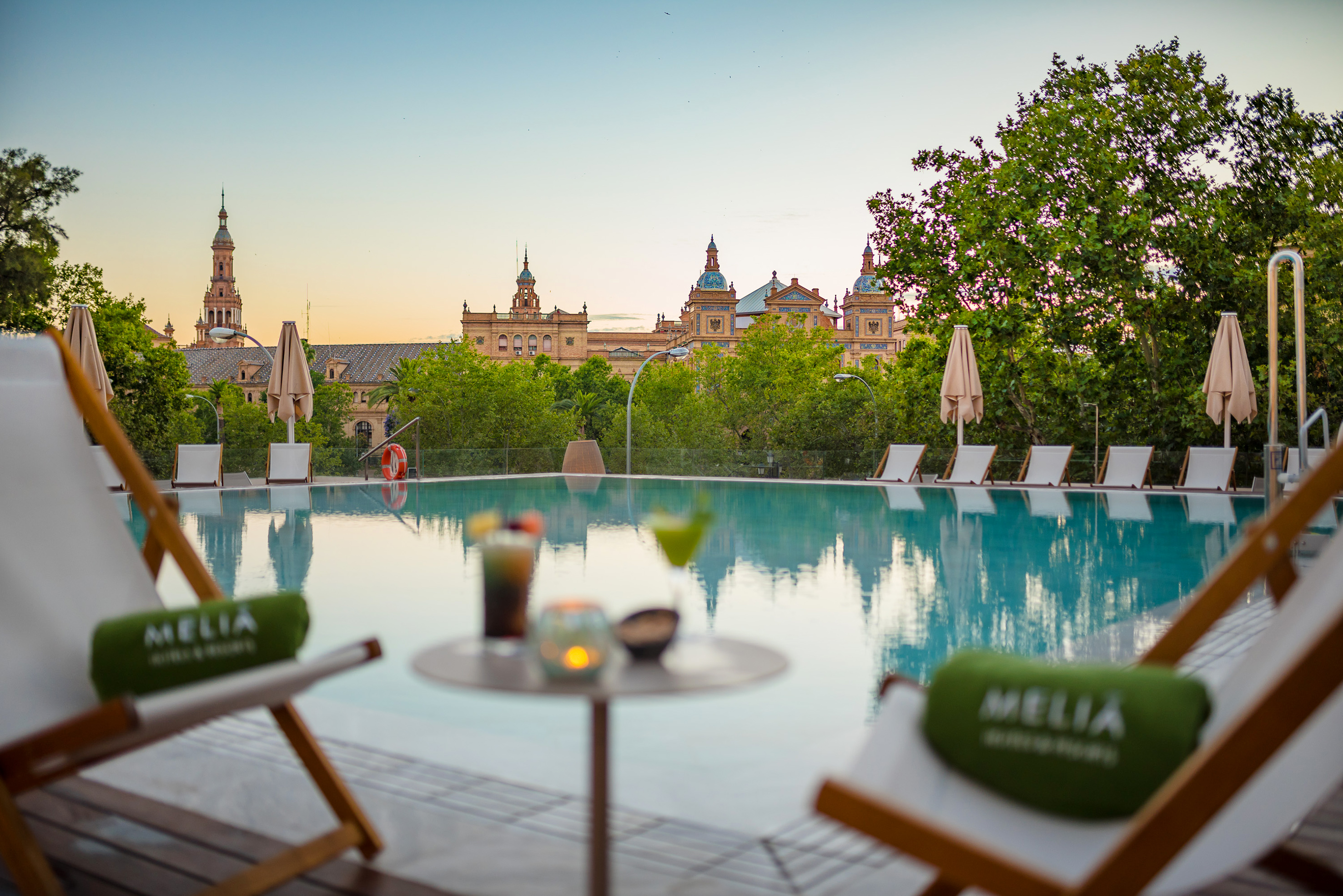 Melia hotel infinity pool, Seville, with cocktails and historic architecture at sunset.