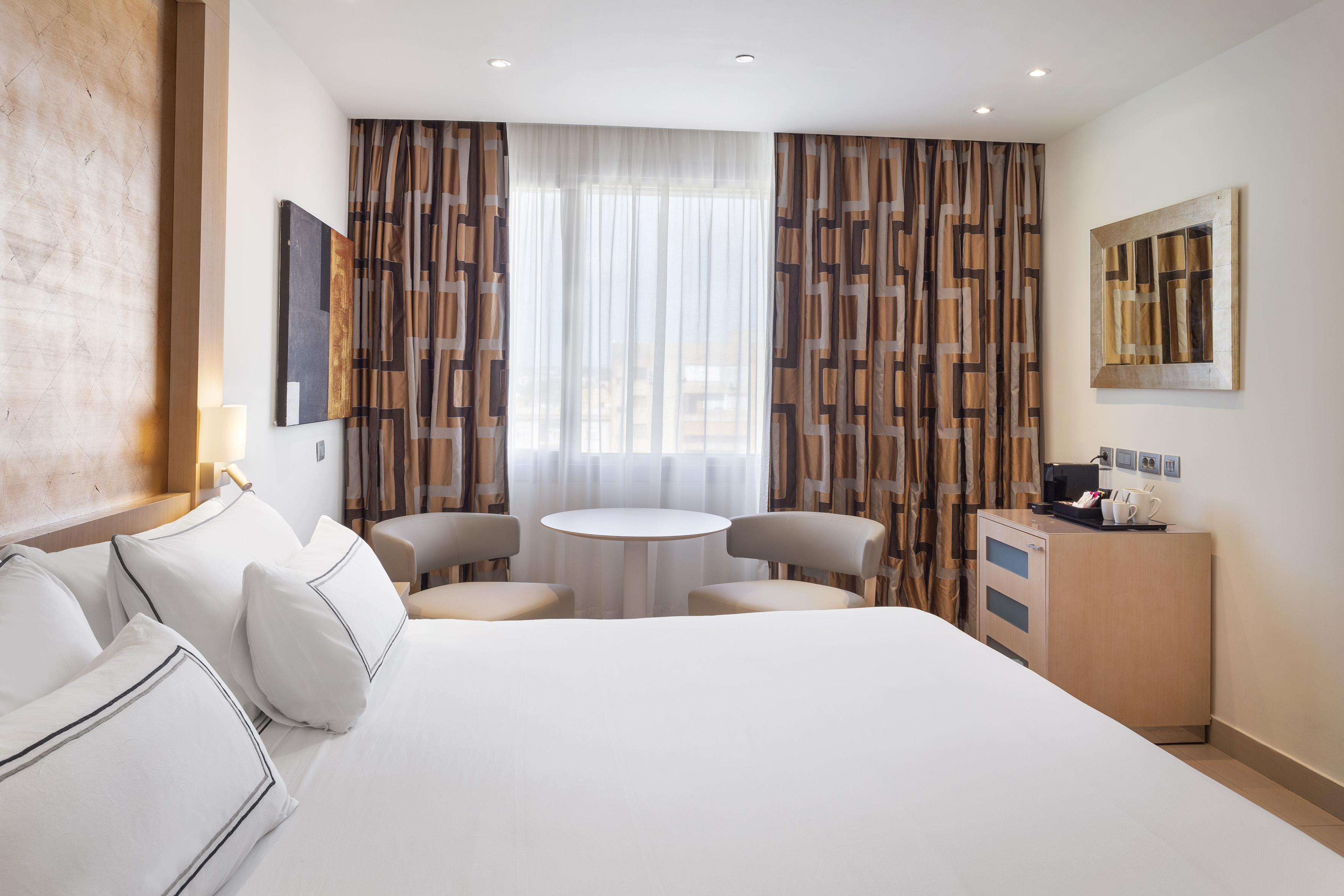 Modern hotel bedroom with king bed, geometric curtains, and coffee station.