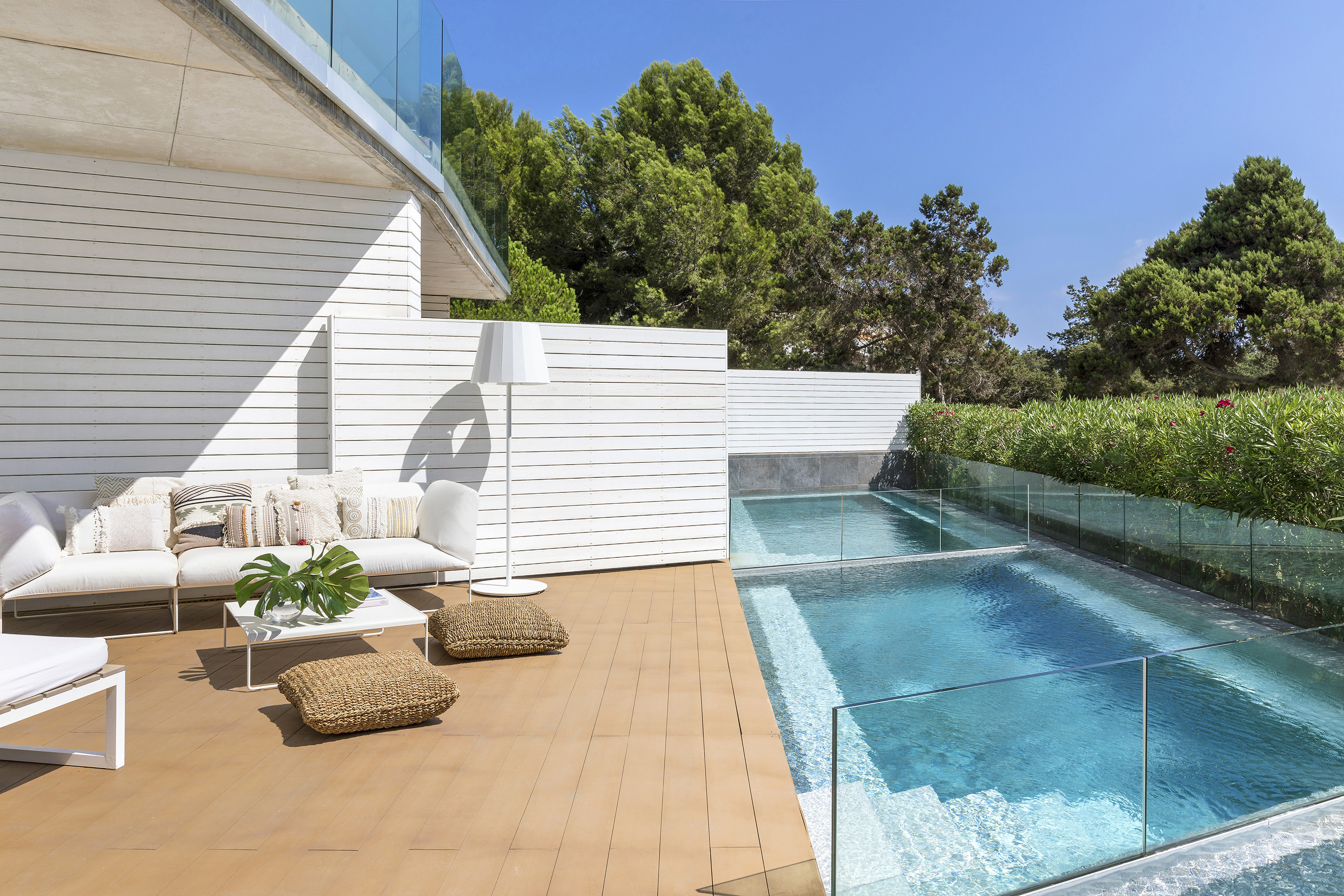 Contemporary patio with white sofa, wooden deck, and glass-fenced pool.