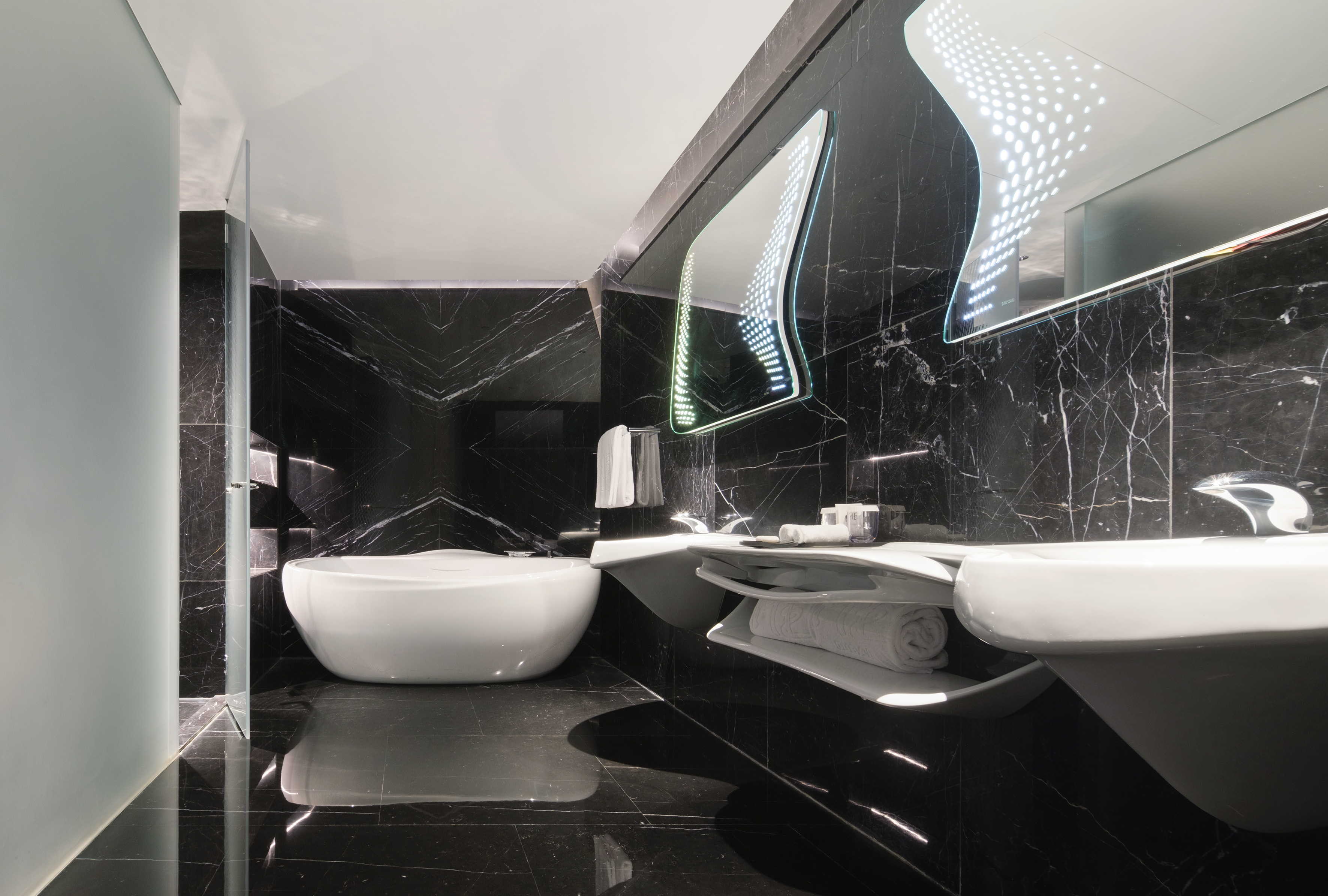 Luxurious modern bathroom with black marble, freestanding tub, and illuminated mirror.