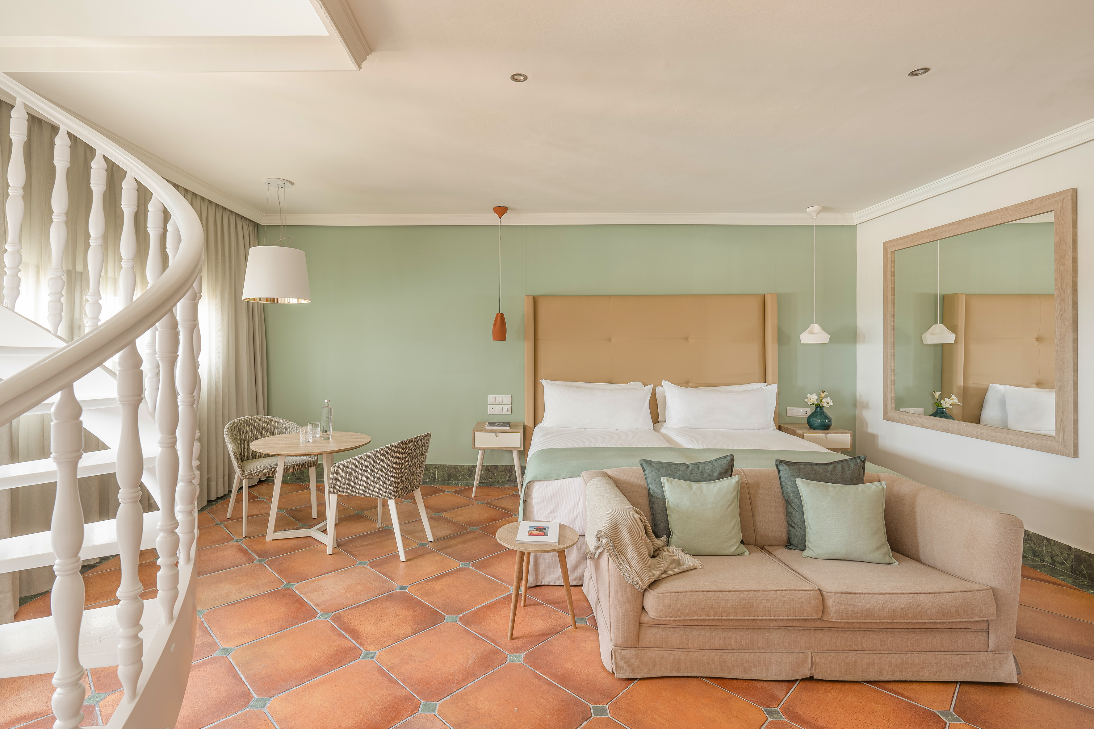 Elegant hotel suite with bed, sofa, spiral staircase, and terracotta floor.