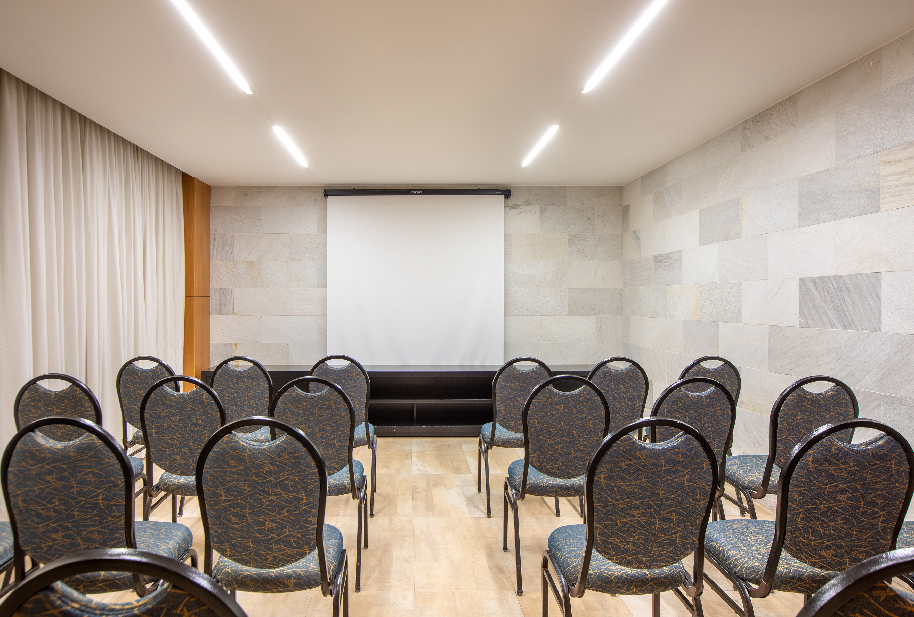 Empty modern meeting room with rows of chairs and a projection screen.