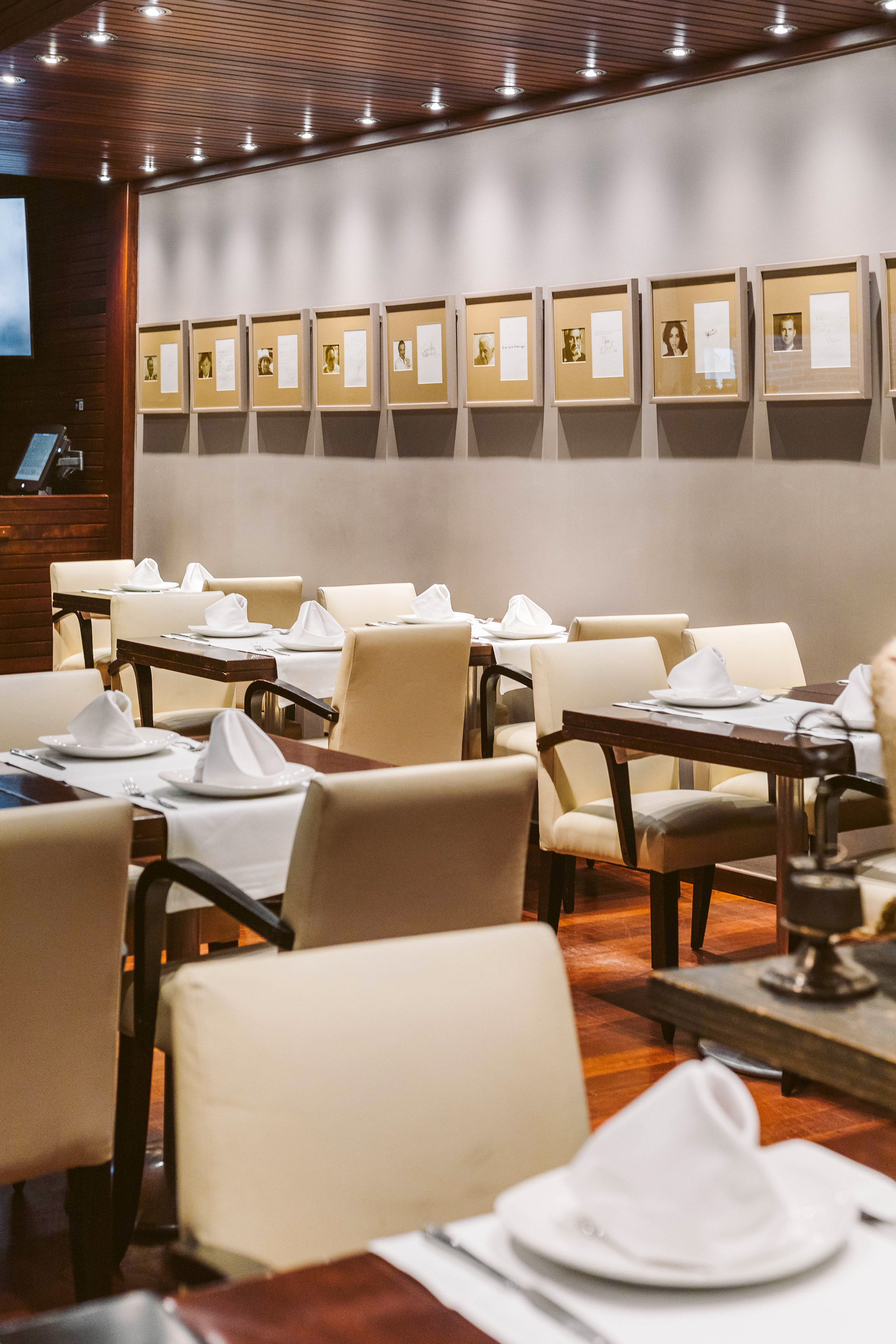 Elegant restaurant dining room with set tables, cream chairs, wood floor, and framed art.