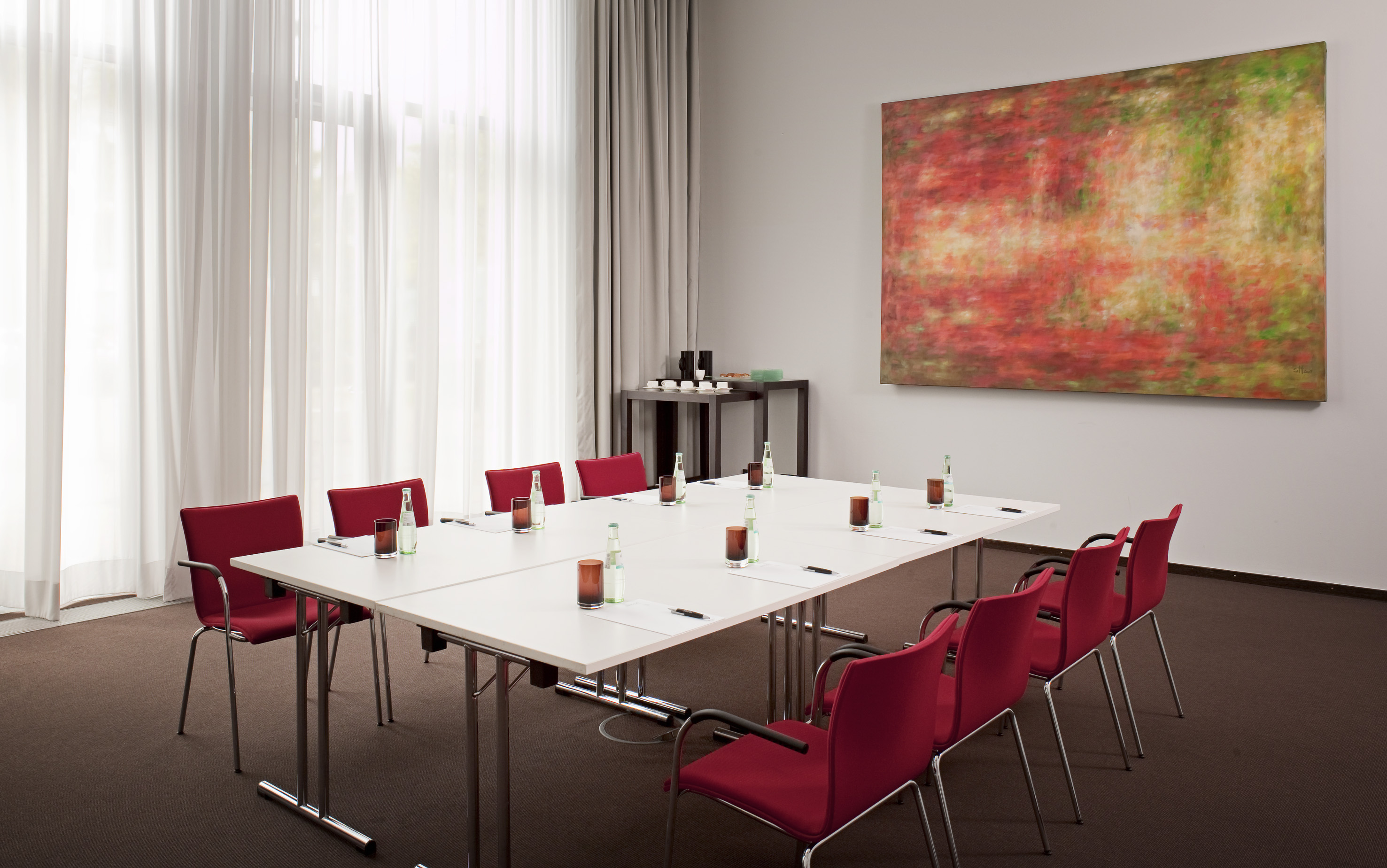 Sleek meeting room with red chairs, white table, and large abstract painting.