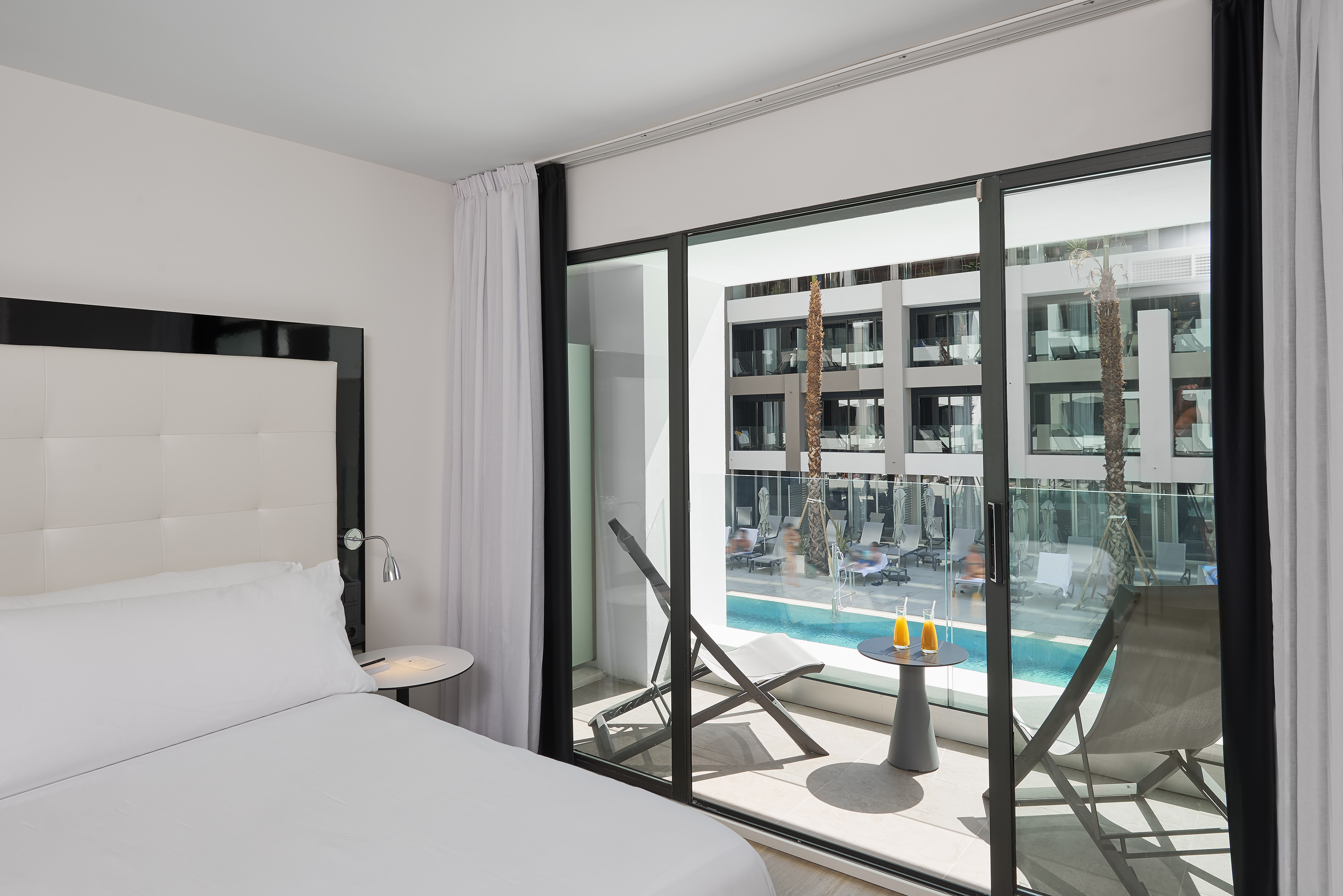 Modern resort room with balcony, pool view, and outdoor lounge area.