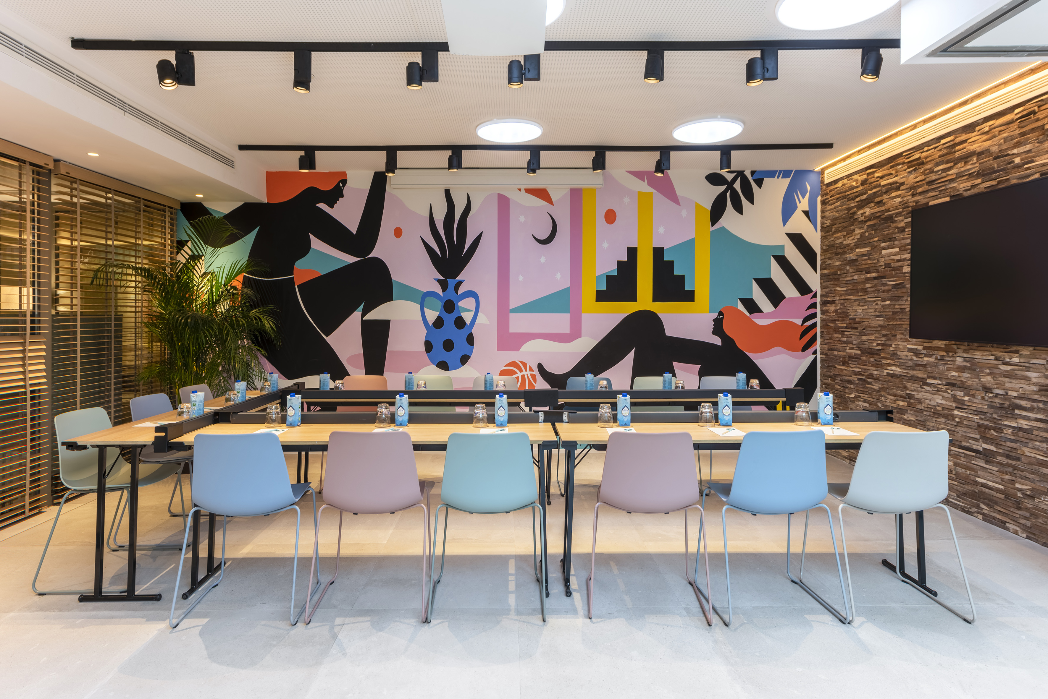 Modern meeting room with colorful chairs, U-table, and vibrant abstract wall mural.