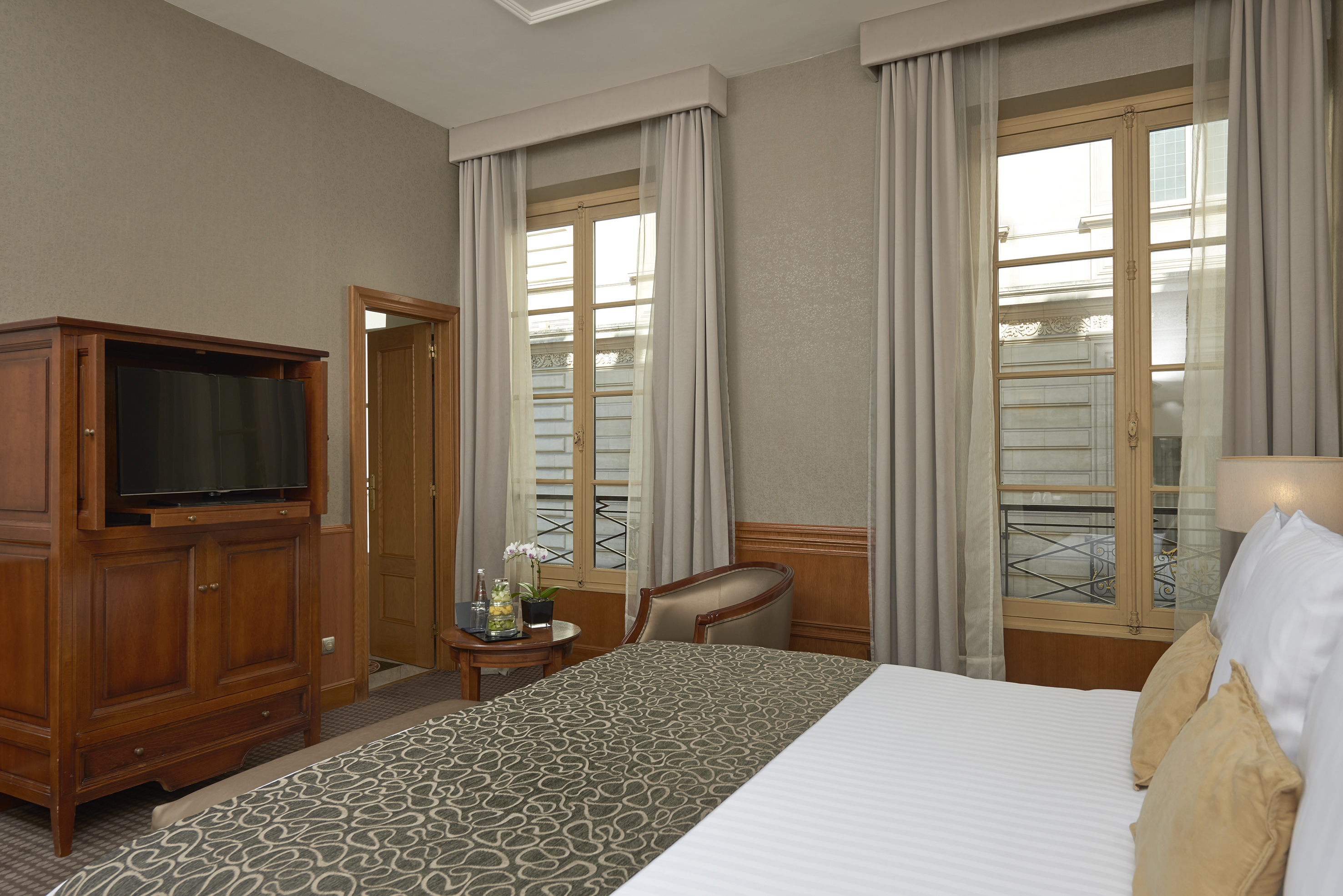 Hotel room with bed, wooden TV cabinet, and tall windows.