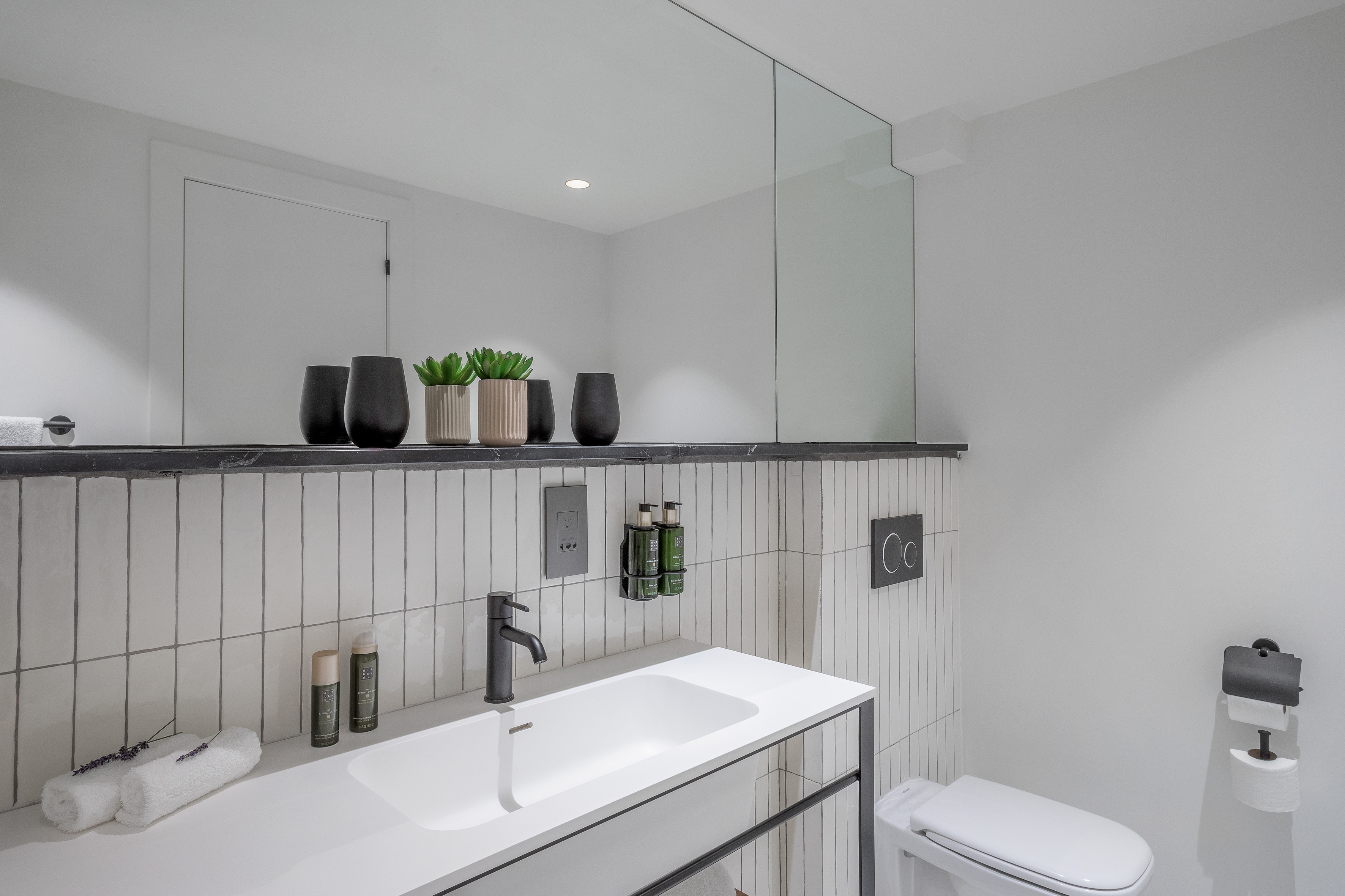Modern white bathroom with black faucet, vanity, toilet, and subway tiles.