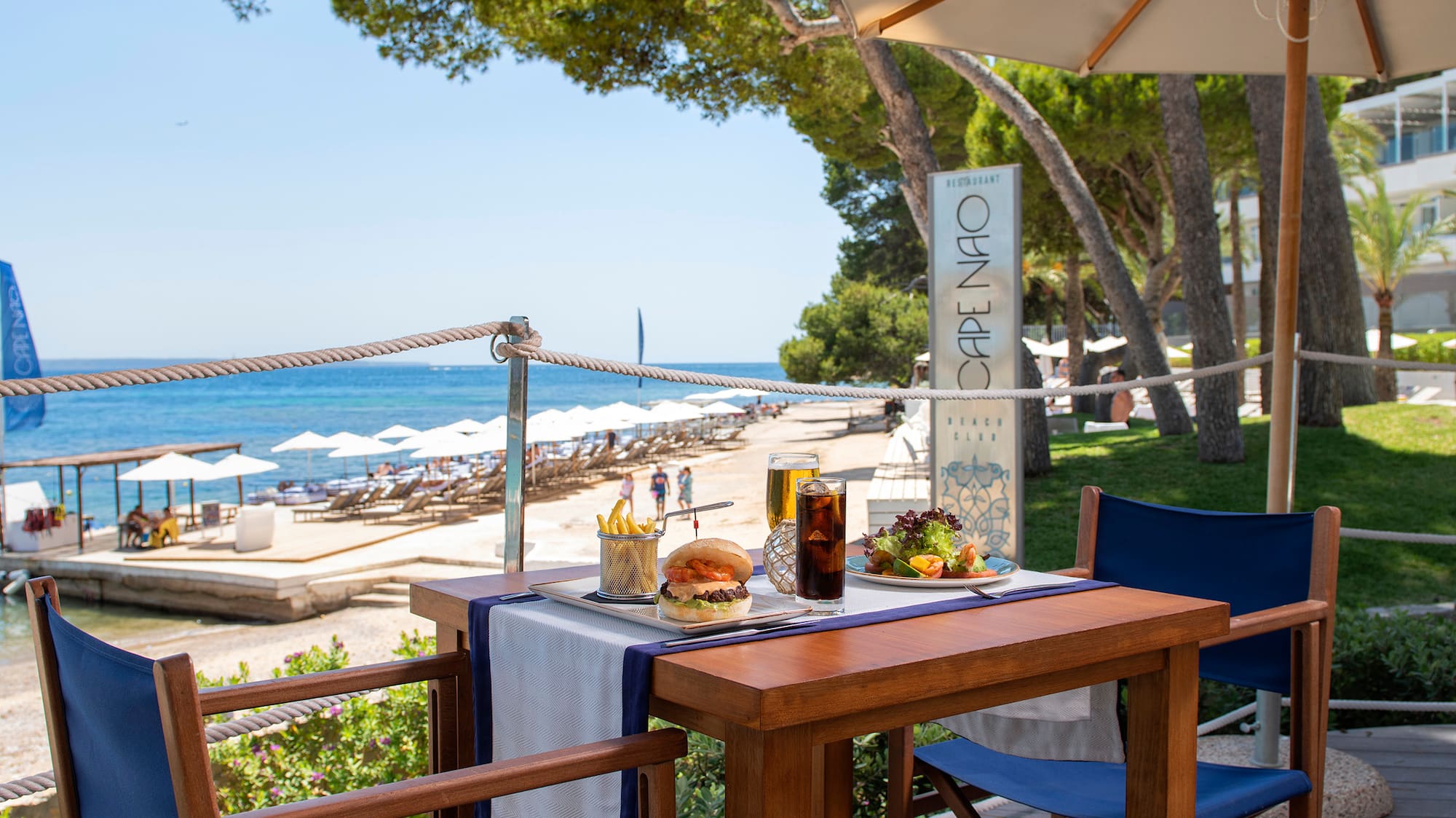 a table with food and drinks on it on a deck with umbrellas and trees