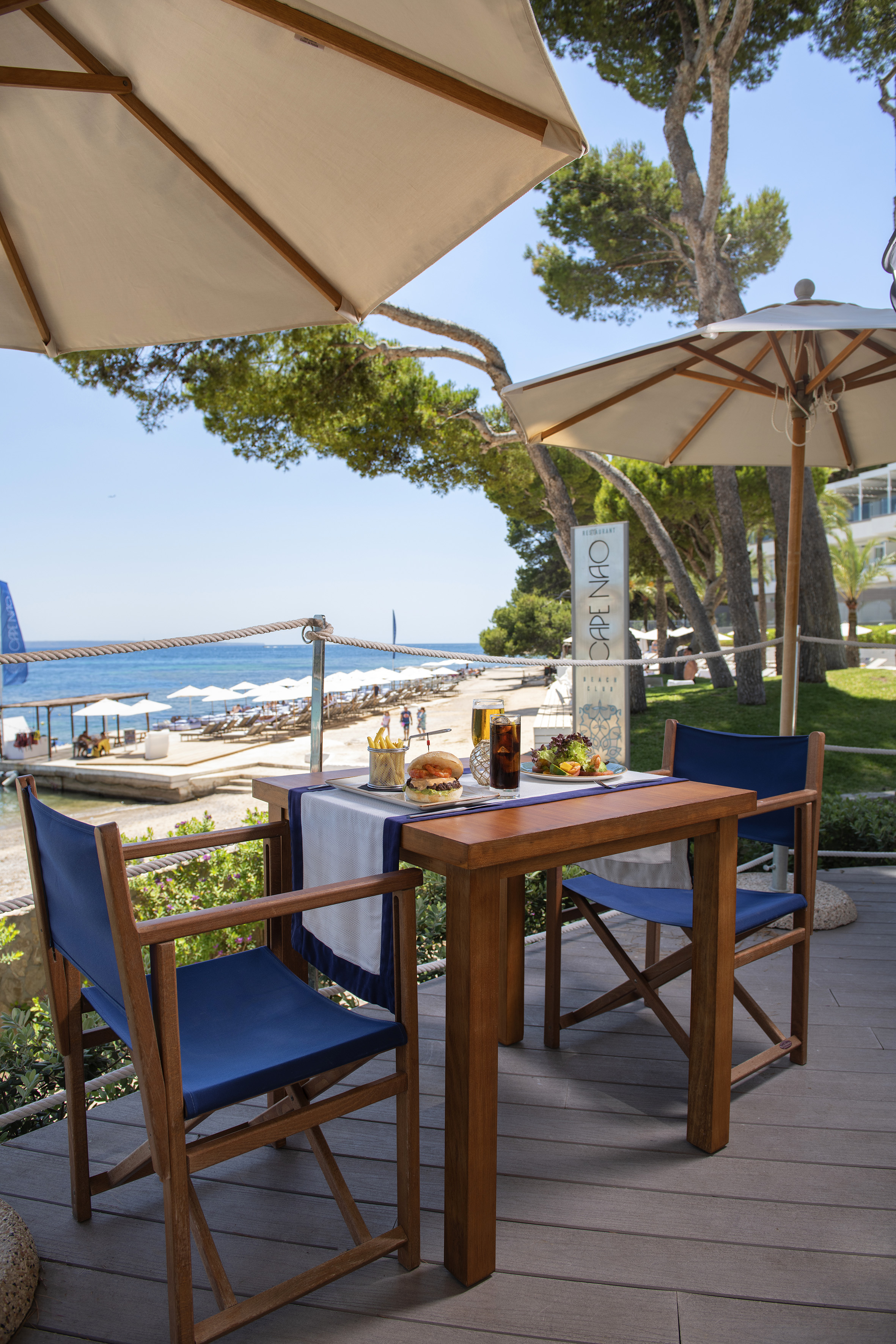 a table with food and drinks on it on a deck with umbrellas and trees