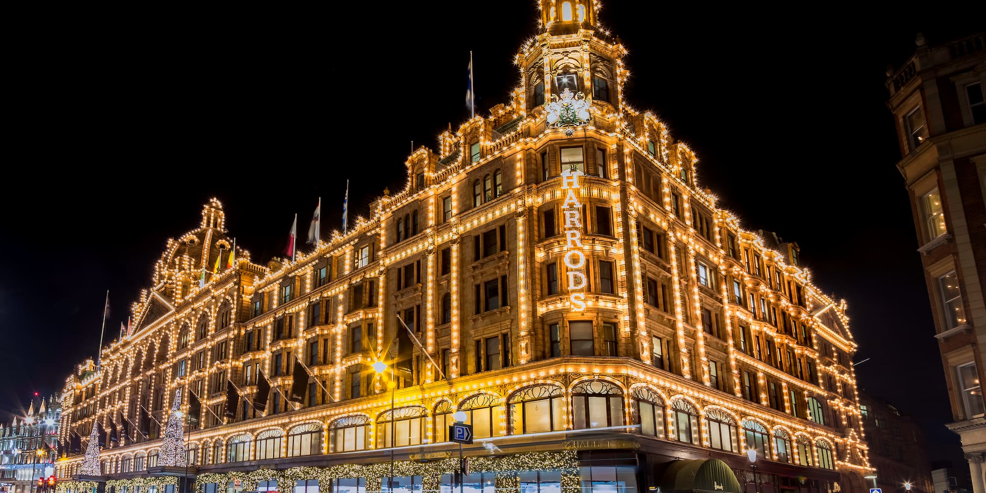 Harrods Londres de noche, edificio iluminado con luces doradas y tráfico.