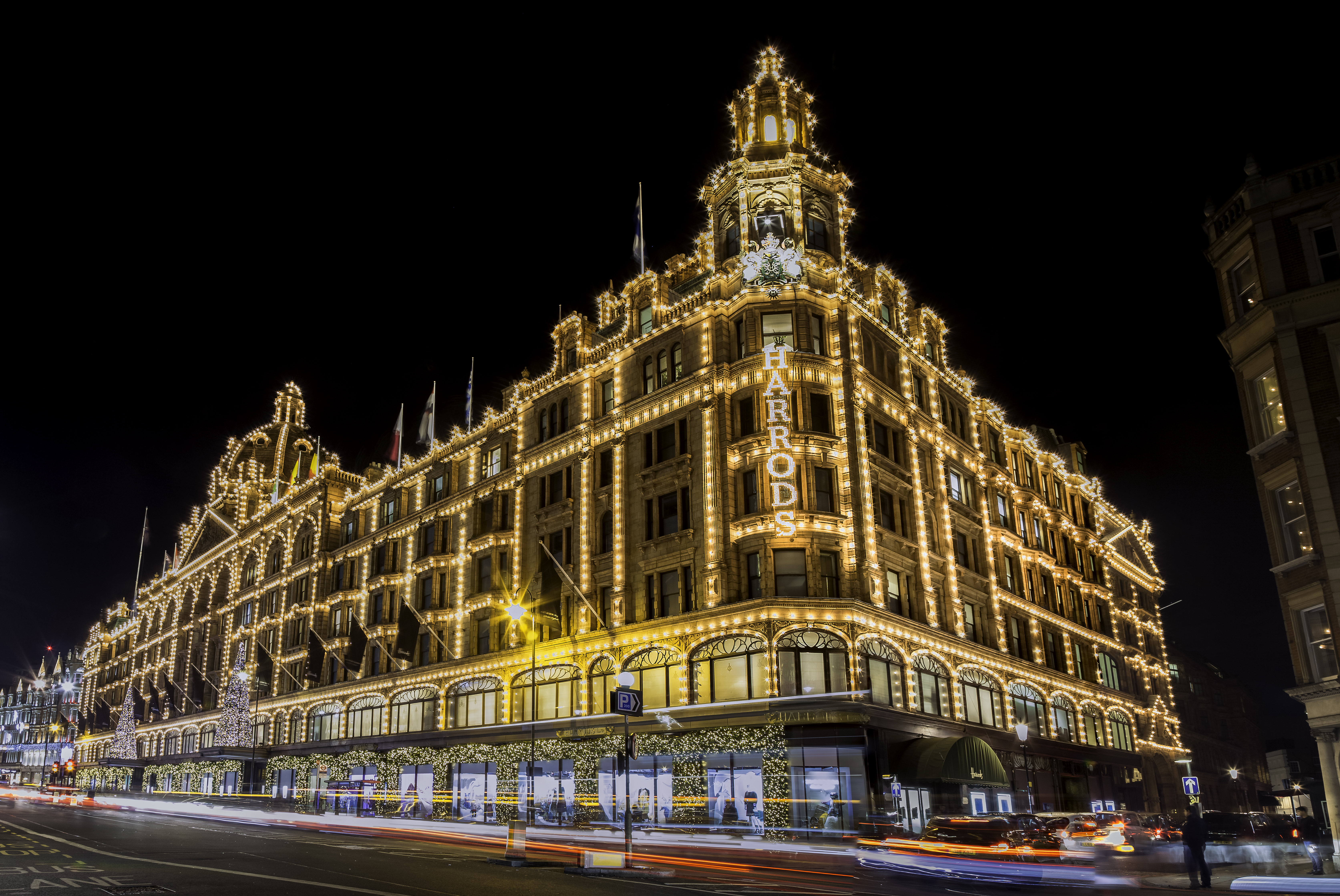 Harrods Londres de noche, edificio iluminado con luces doradas y tráfico.