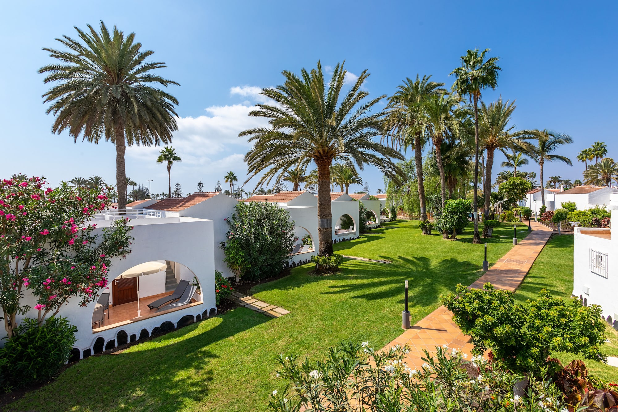 Tropical resort bungalows with terraces, palm trees, and green gardens.