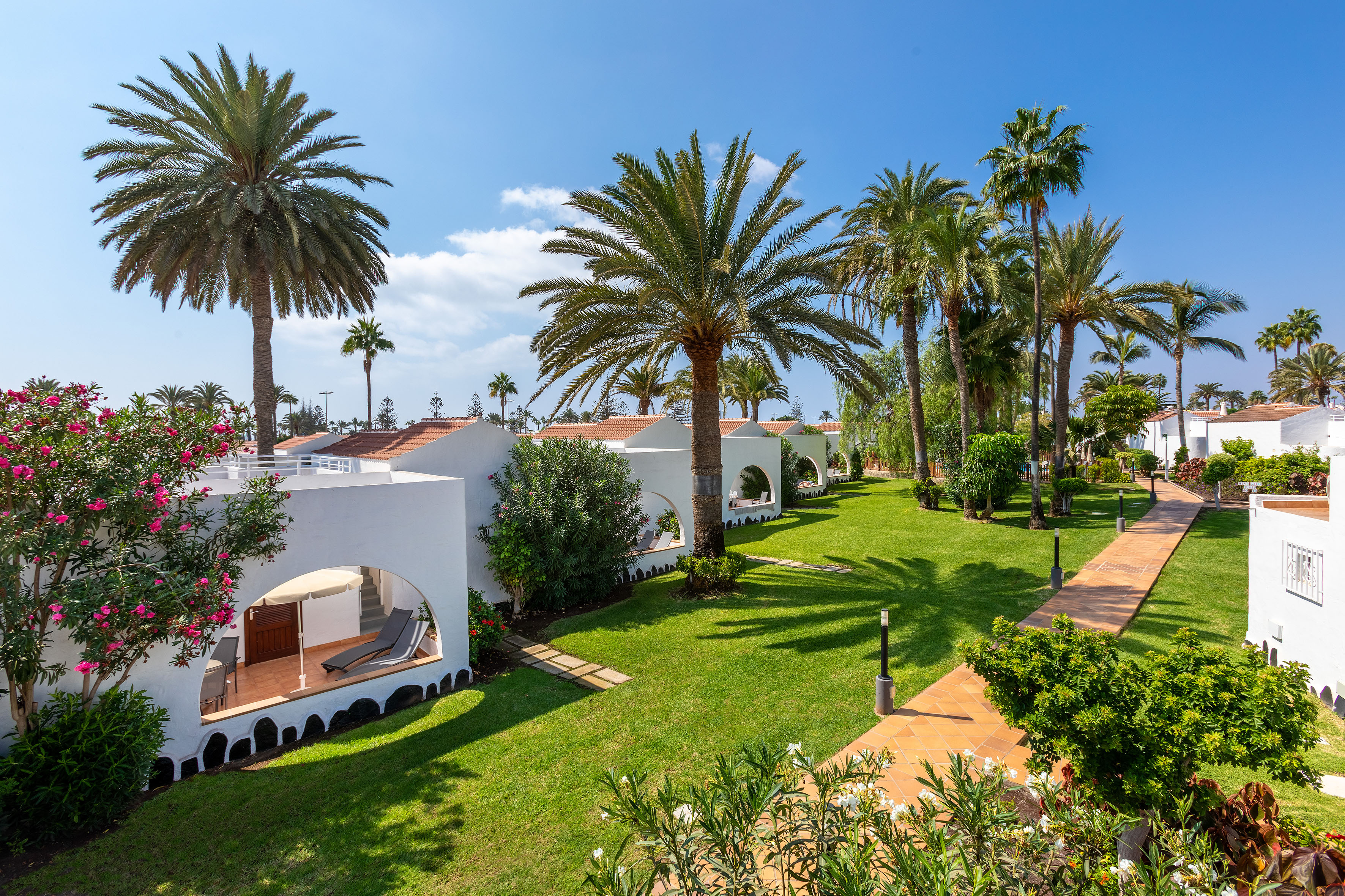 Tropical resort bungalows with terraces, palm trees, and green gardens.