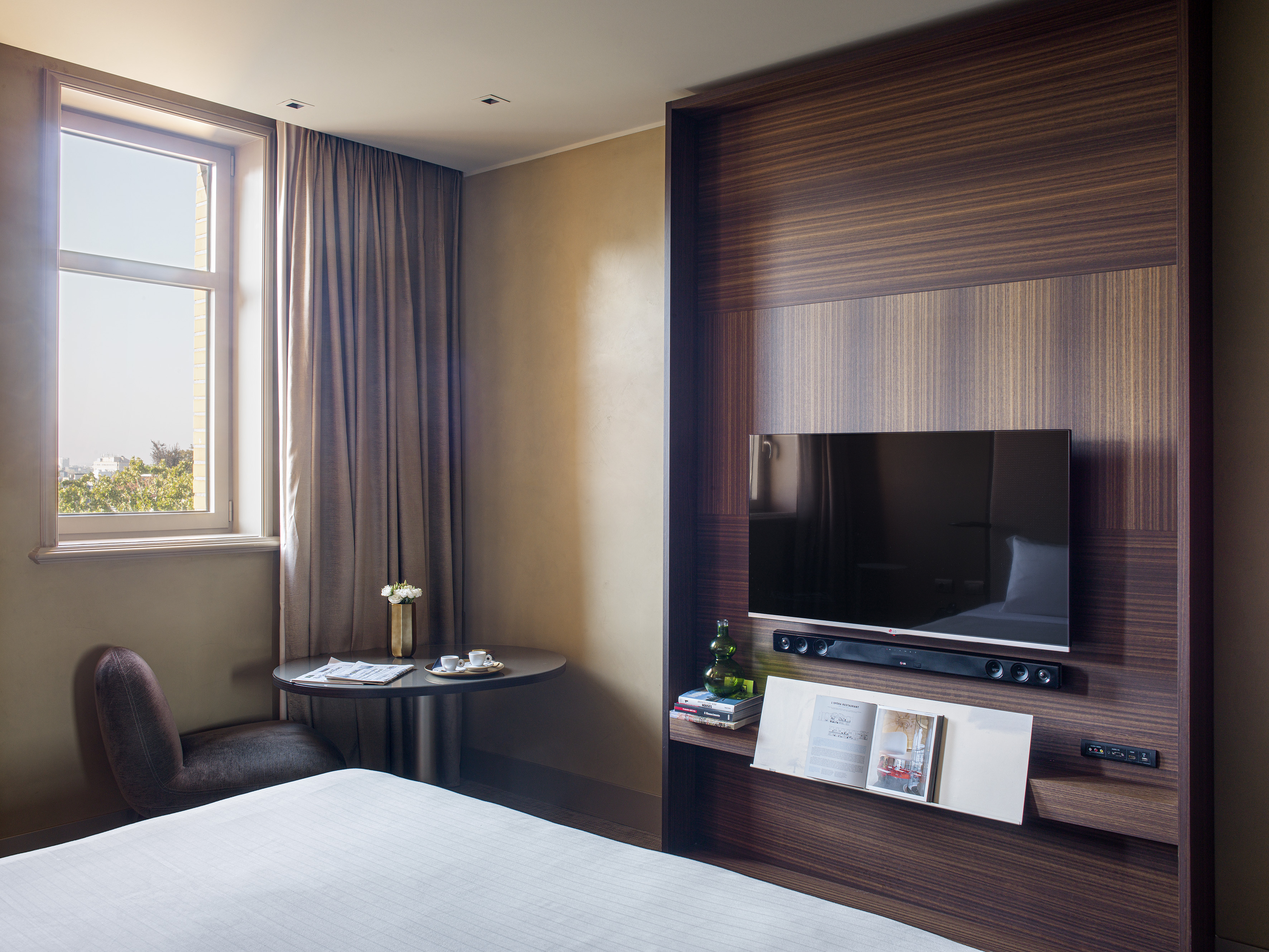 Modern hotel room with bed, window, integrated TV, and a small table.