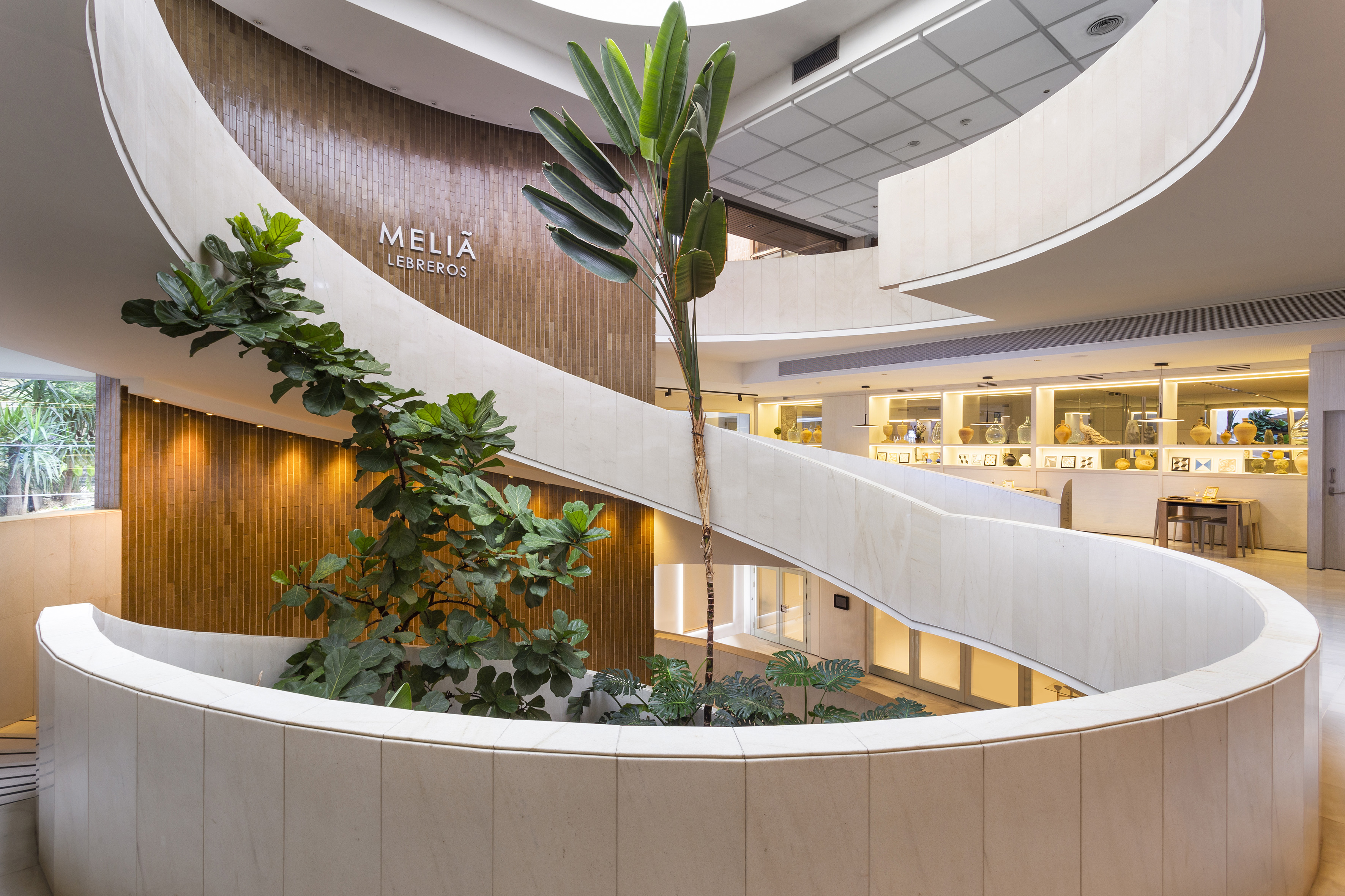Meliã Lebreros hotel lobby atrium with curved balconies, lush plants, and modern design.