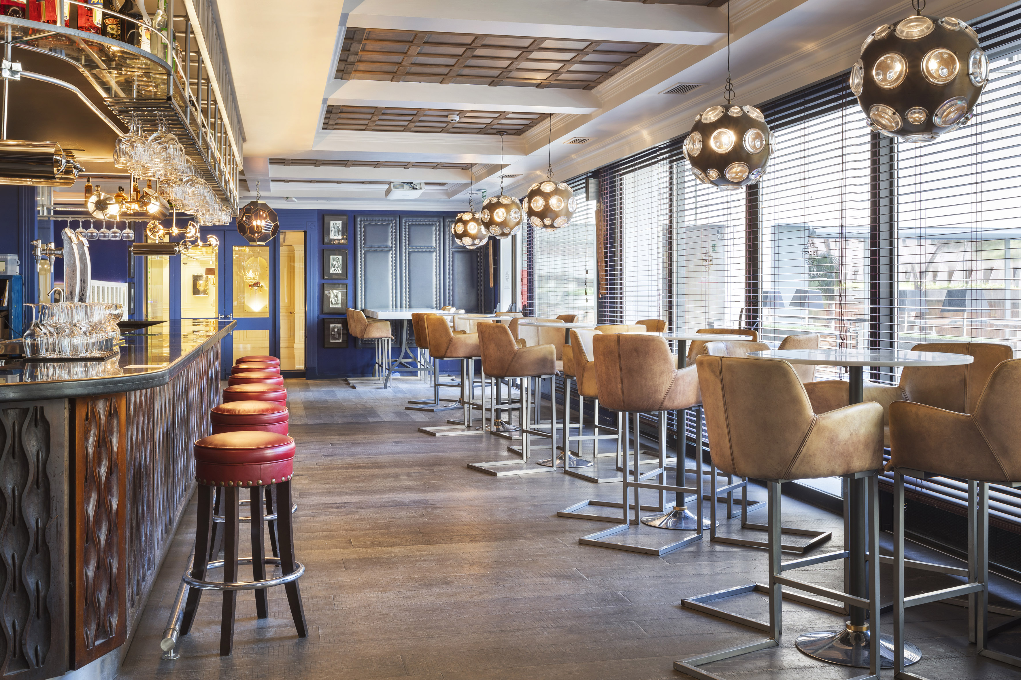Stylish blue bar lounge, red stools, brown chairs, wood floor, pendant lights.