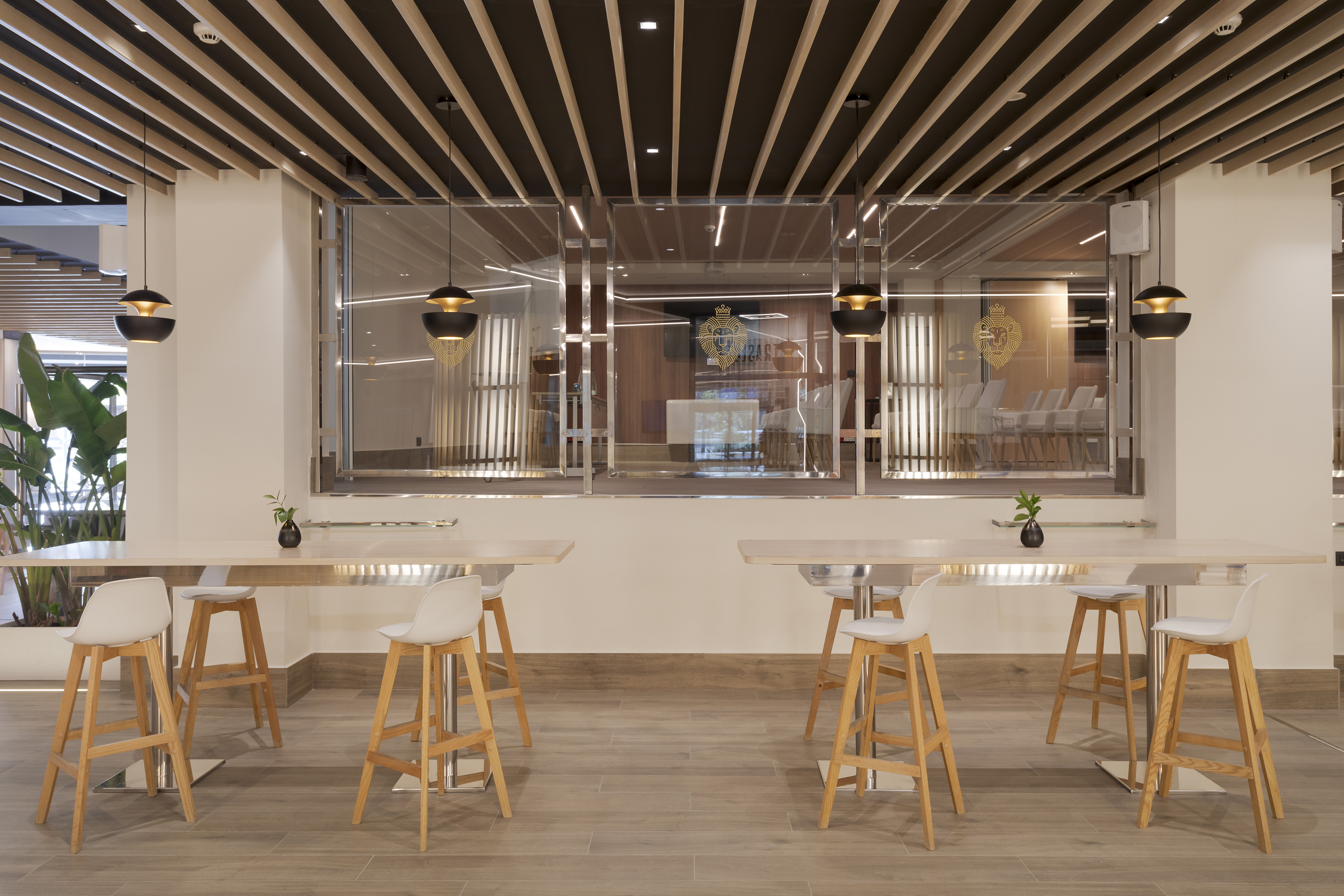 Modern lounge with high tables, white bar stools, and wood slat ceiling.