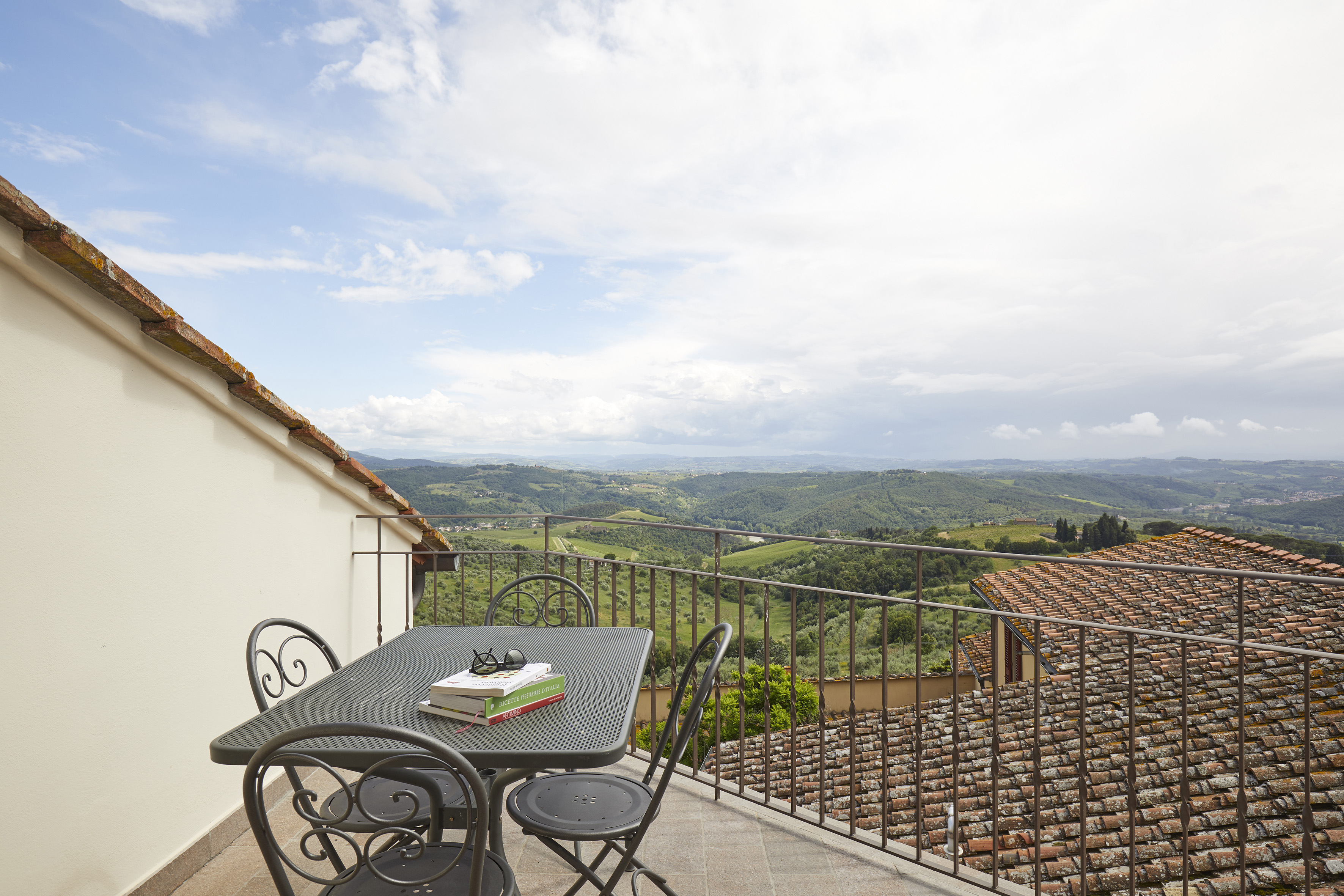 Balcony with table, books, overlooking green countryside and tiled roofs.