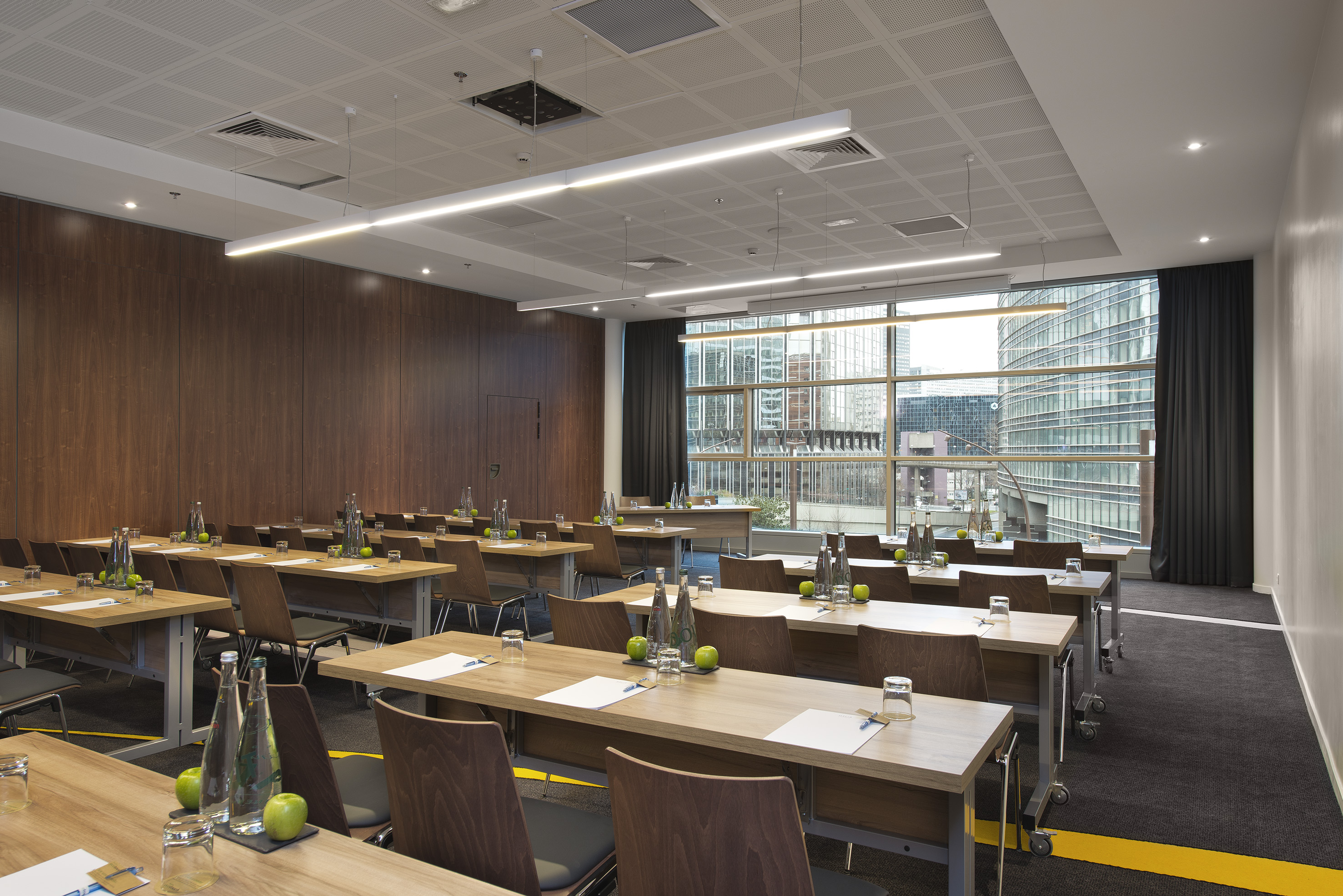 Bright training room with rows of wooden tables, city view, and prepared settings.
