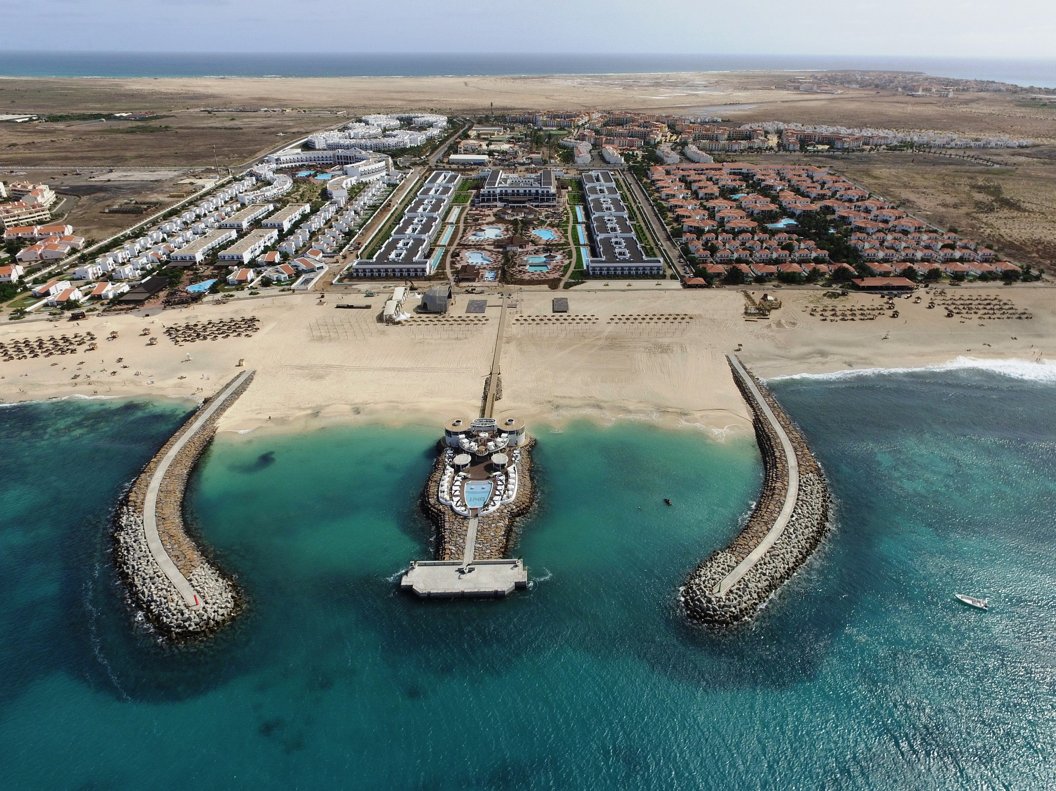 Resort de playa con rompeolas, muelle con piscina y aguas turquesas.
