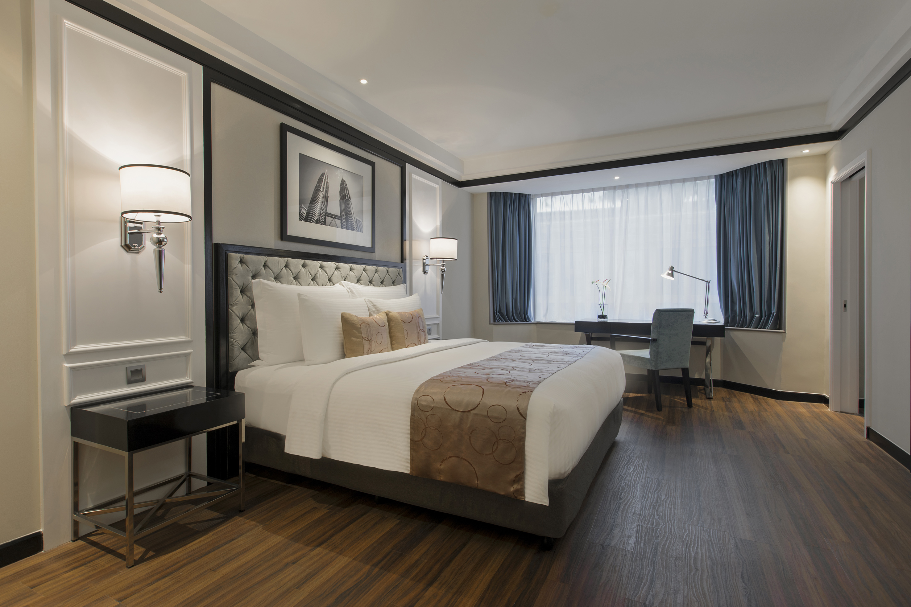 Luxury hotel bedroom with bed, desk by window, and Petronas Towers artwork.